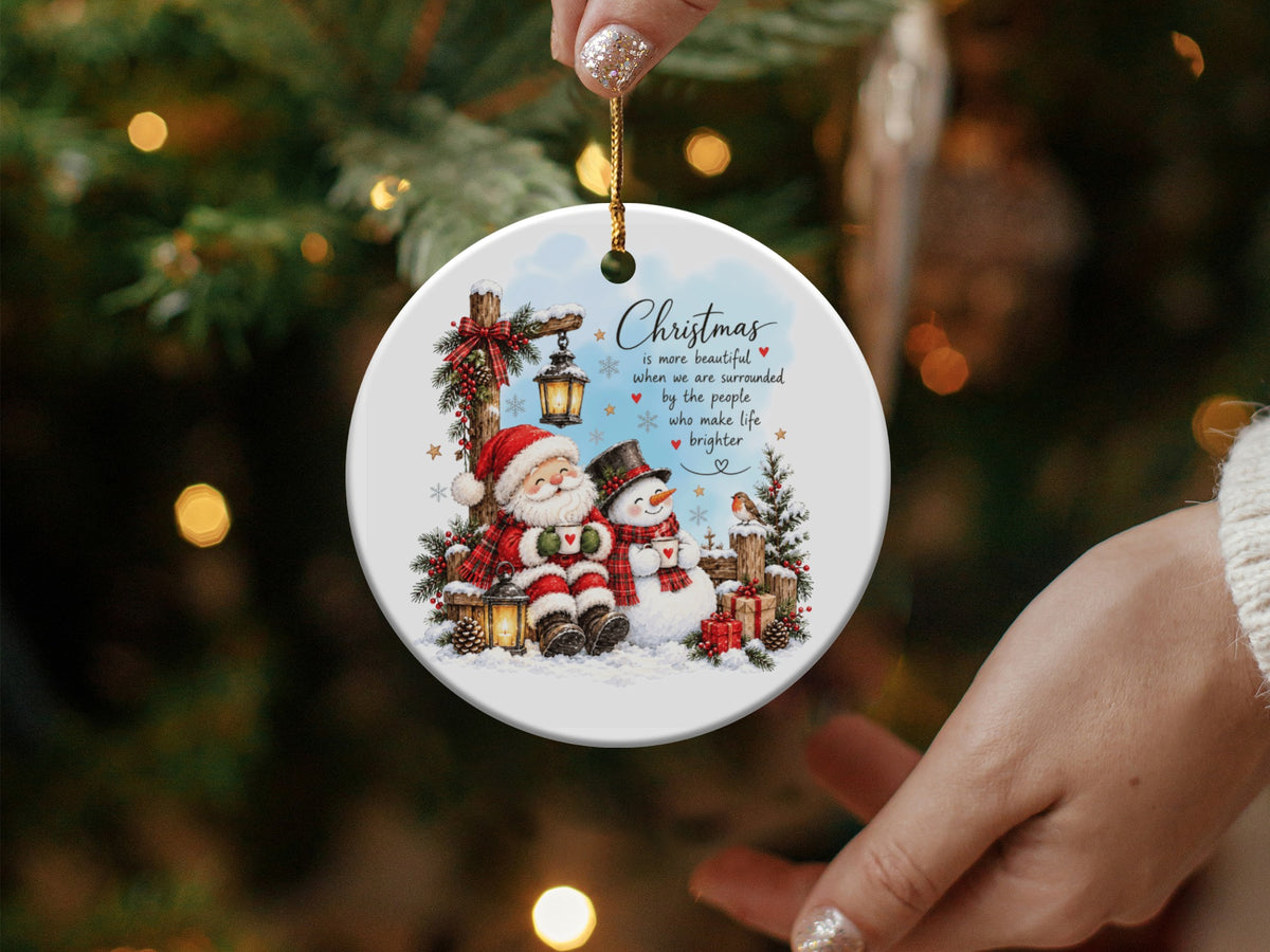 A round white ceramic Christmas ornament featuring Santa, a snowman, and an inspirational holiday message.