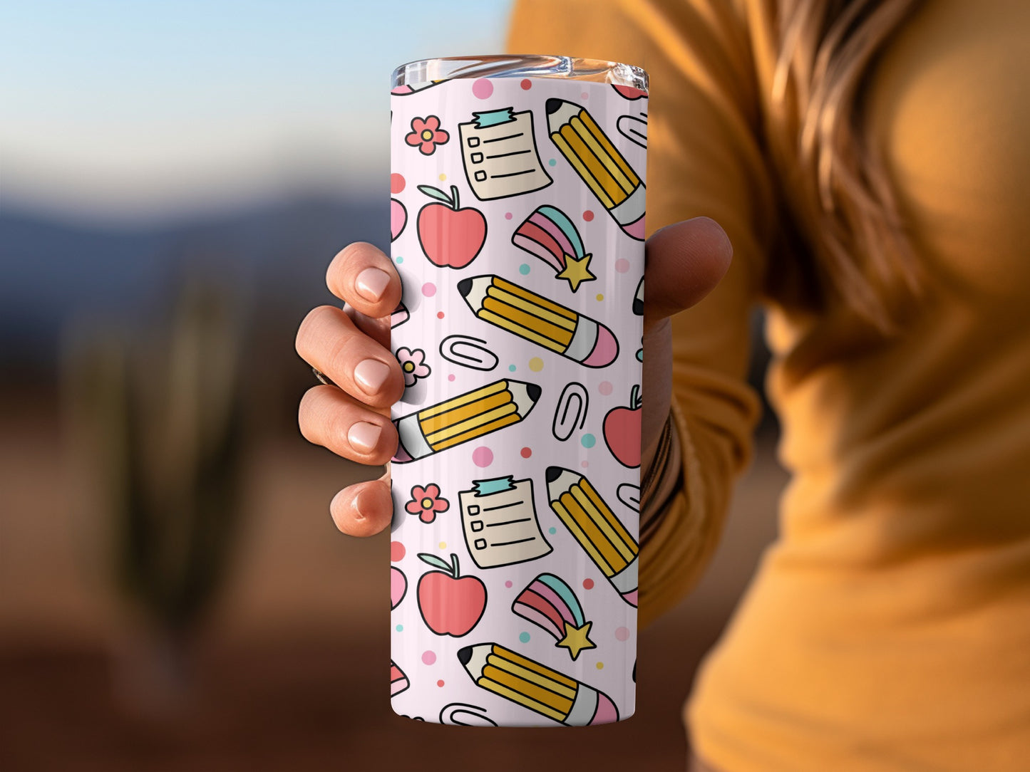 Tumbler with a pink background featuring a doodle pattern of apples, pencils, and notebooks.