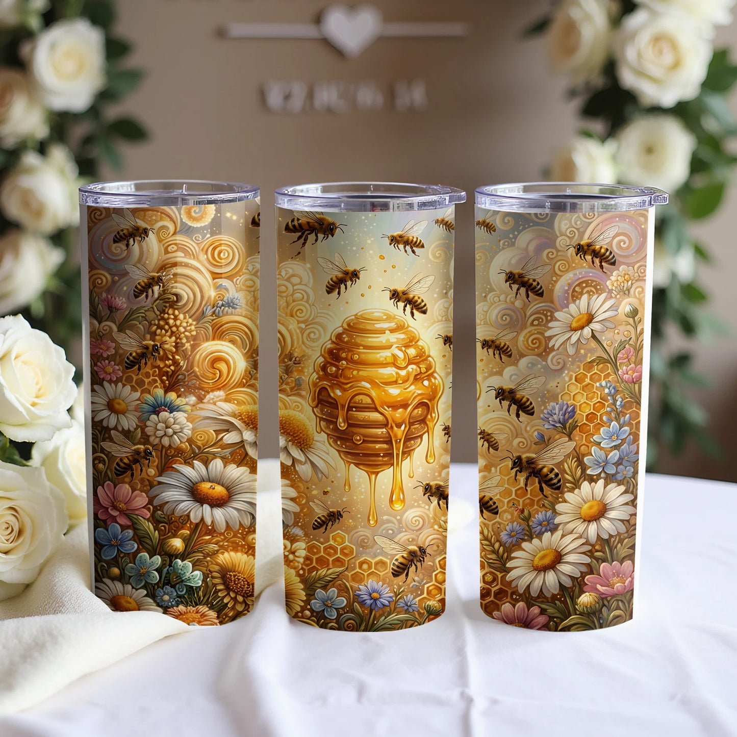 Three tumblers with bees, honeycomb, and flowers, displayed on a white cloth with blurred roses.