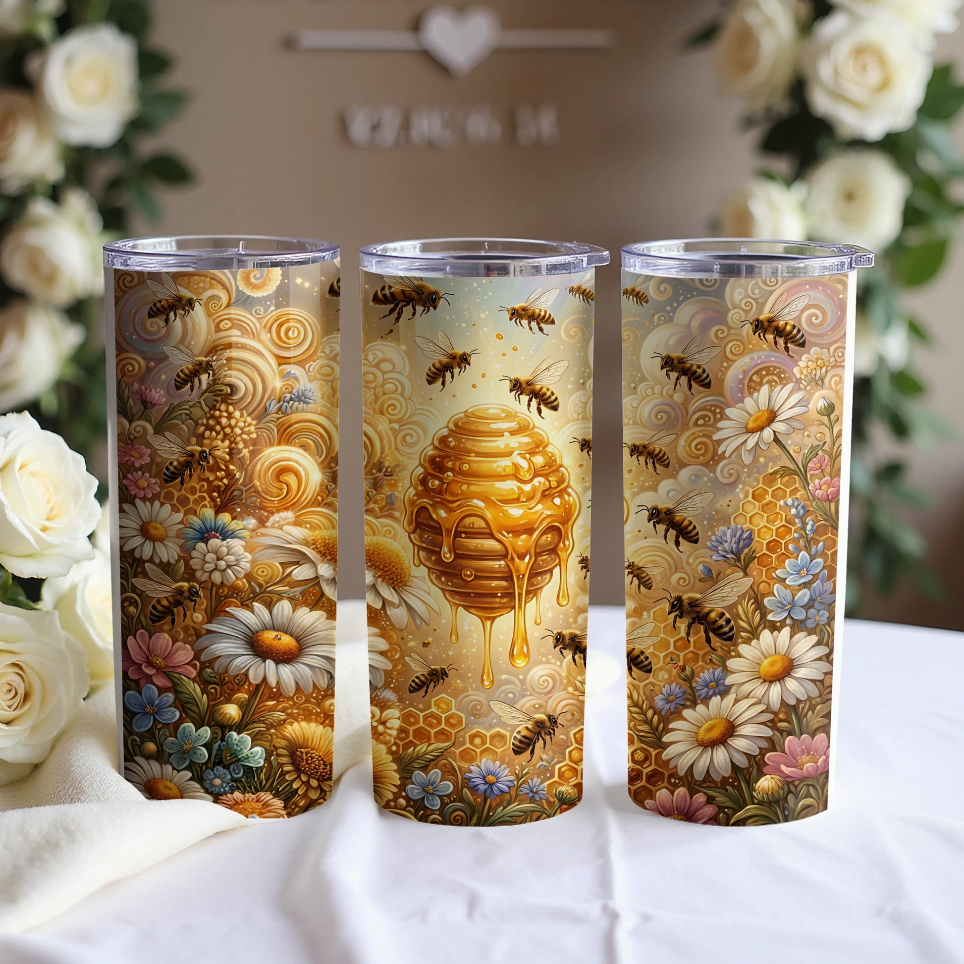 Three tumblers with bees, honeycomb, and flowers, displayed on a white cloth with blurred roses.