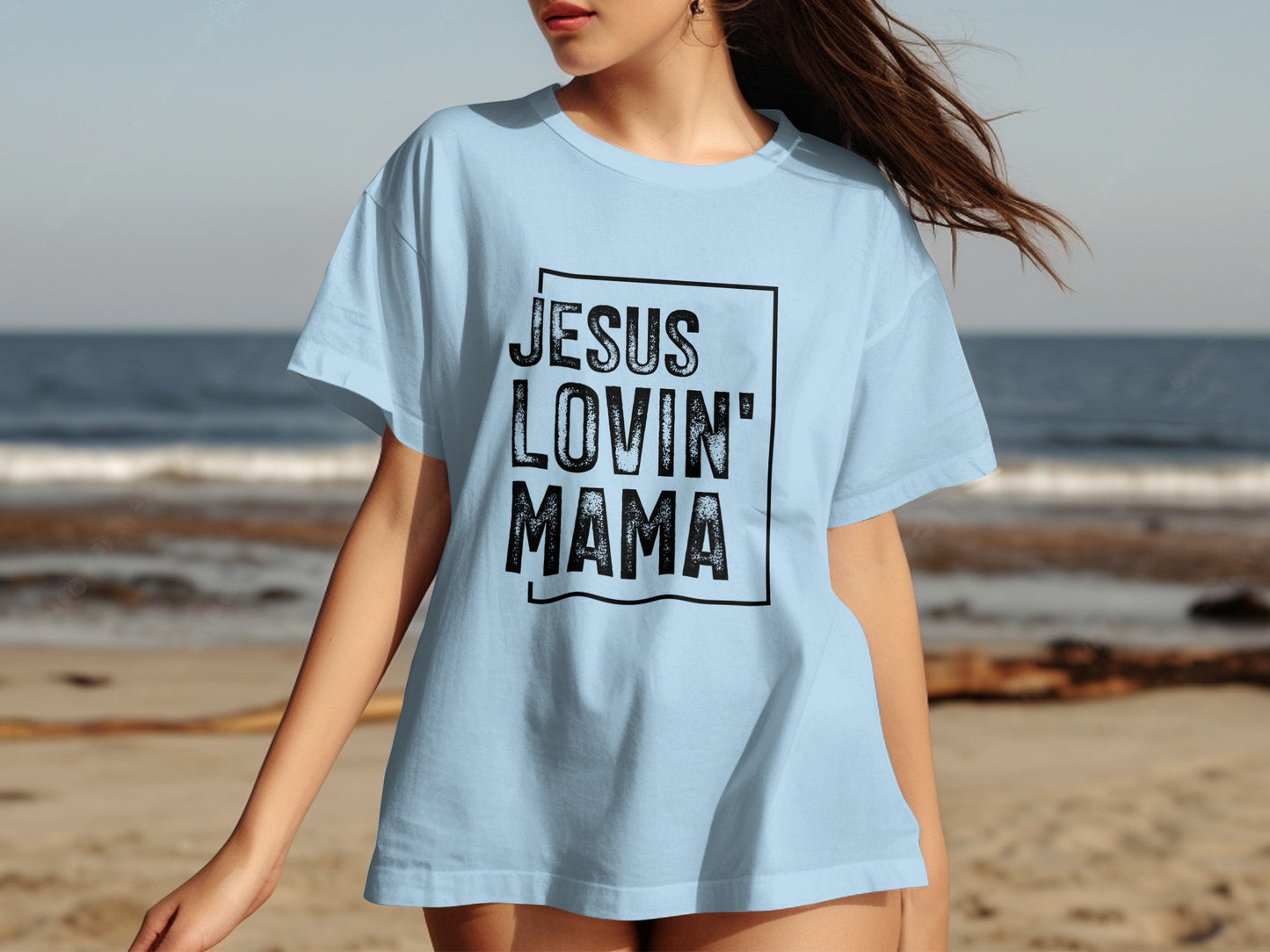 Light blue t-shirt with black text "JESUS LOVIN' MAMA" on a beach background.