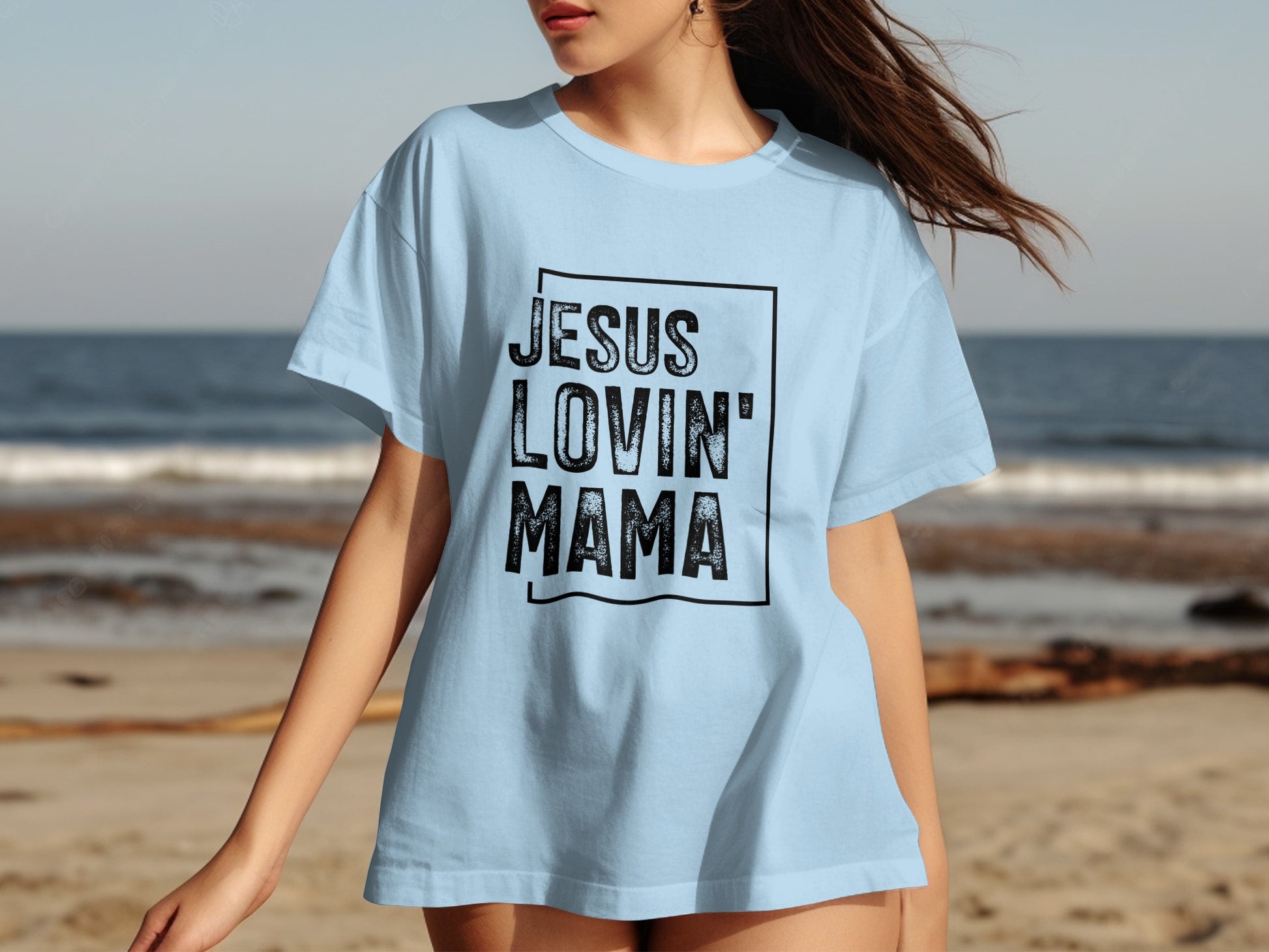Light blue t-shirt with black text "JESUS LOVIN' MAMA" on a beach background.