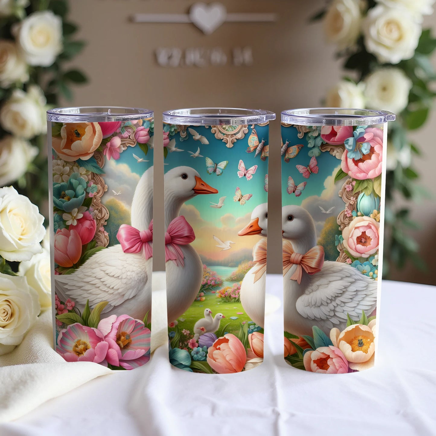 Three tumblers featuring ducks, flowers, and butterflies on a white cloth.