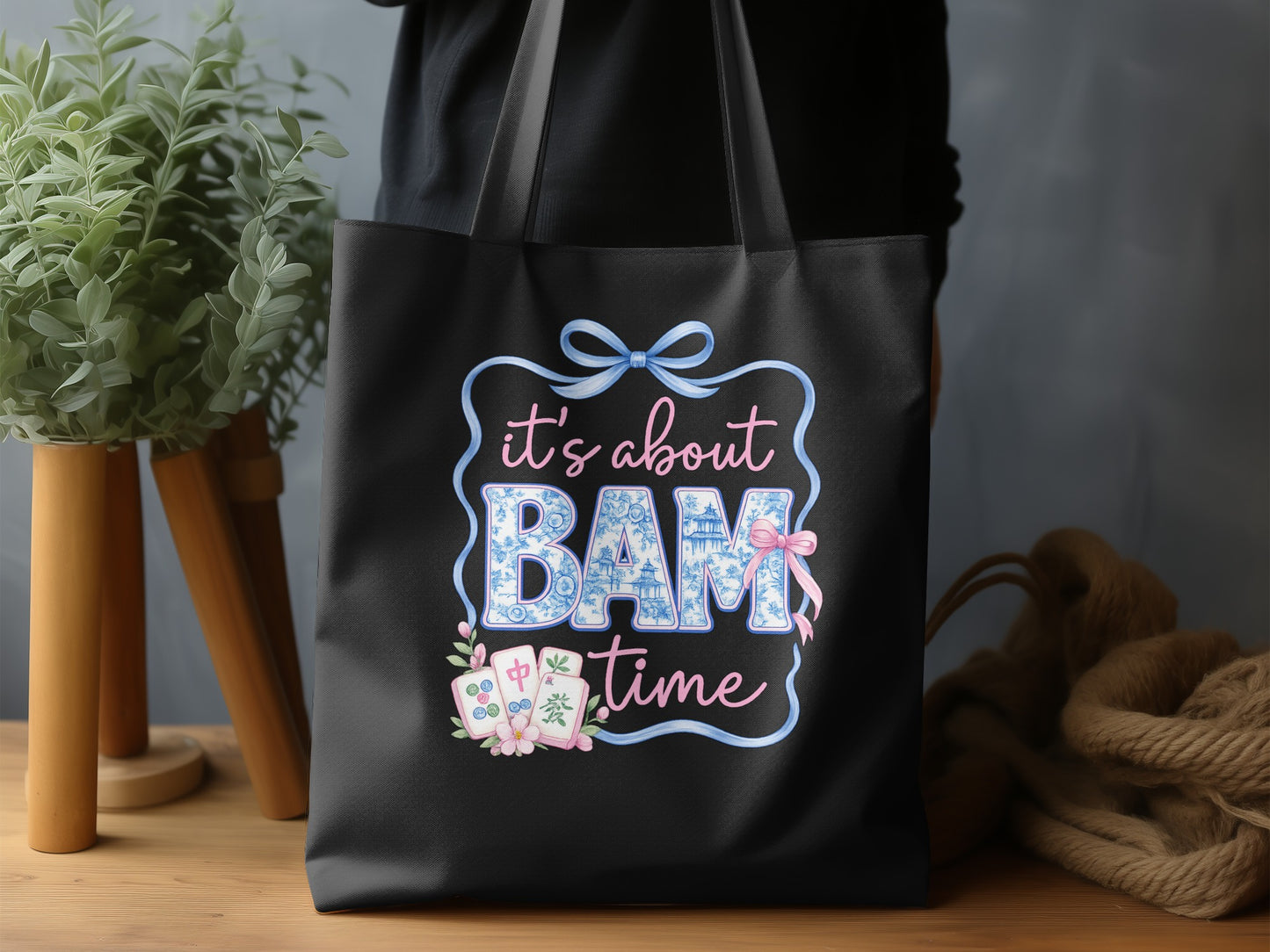 Black tote bag with "it's about BAM time" text in decorative font and mahjong tiles.