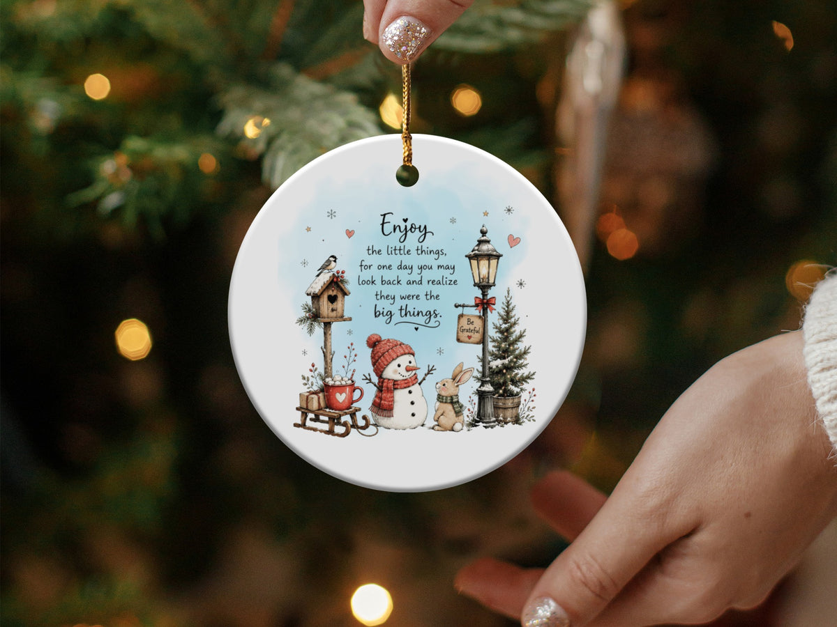 Round white ceramic Christmas ornament featuring a winter illustration with a snowman, bunny, and inspirational quote.