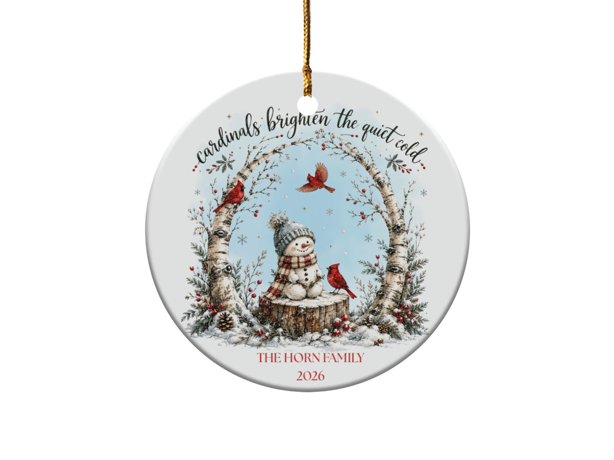 Round ceramic holiday ornament featuring a snowman, red cardinals, birch branches, text reading cardinals brighten the quiet cold, and customizable text.