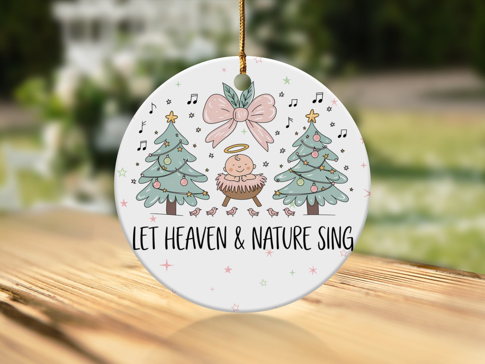 Christmas ornament with baby Jesus, trees, and "Let Heaven & Nature Sing" text.