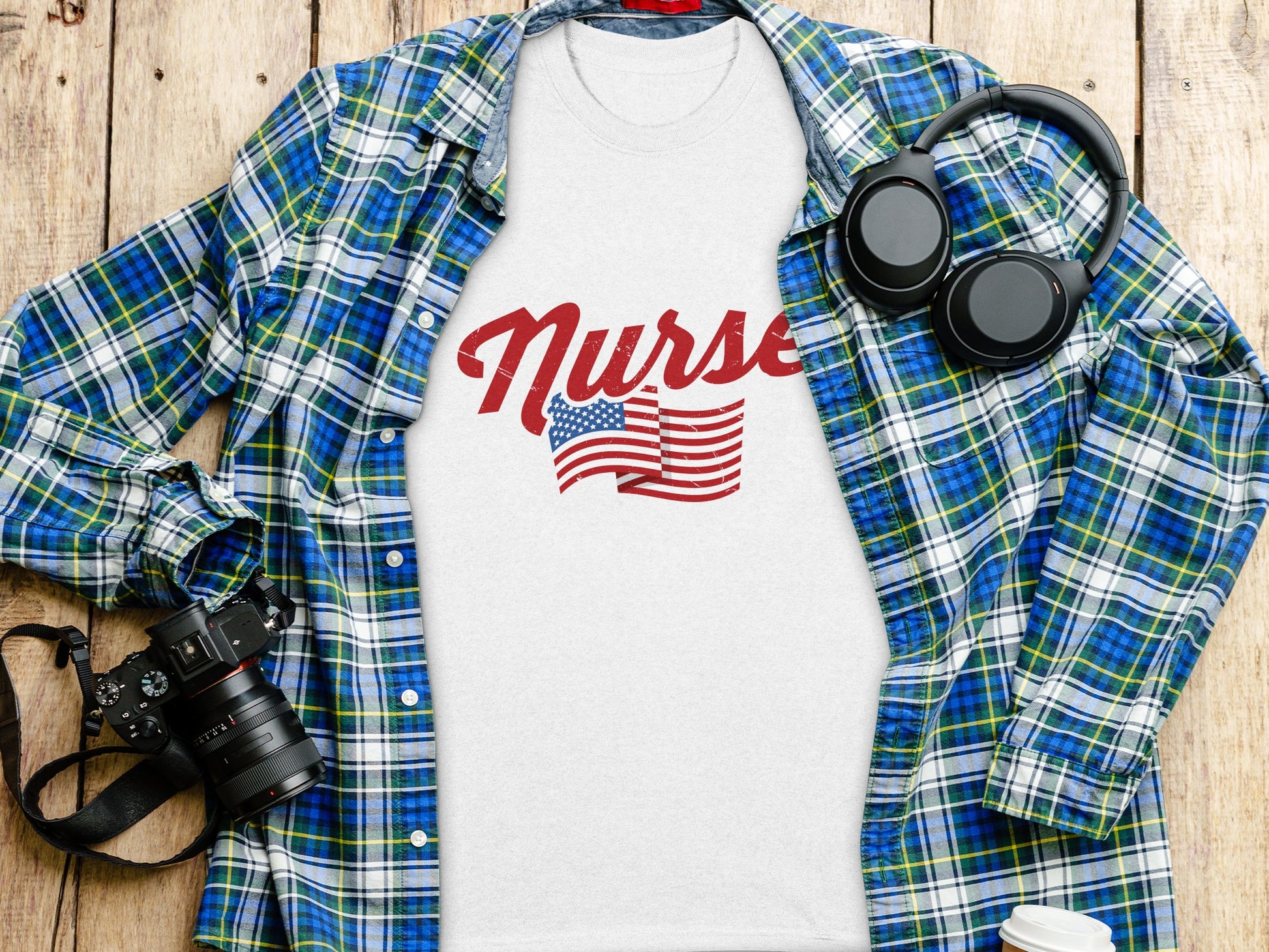 White t-shirt with "Nurse" and American flag graphic, laid flat with a flannel shirt and headphones.