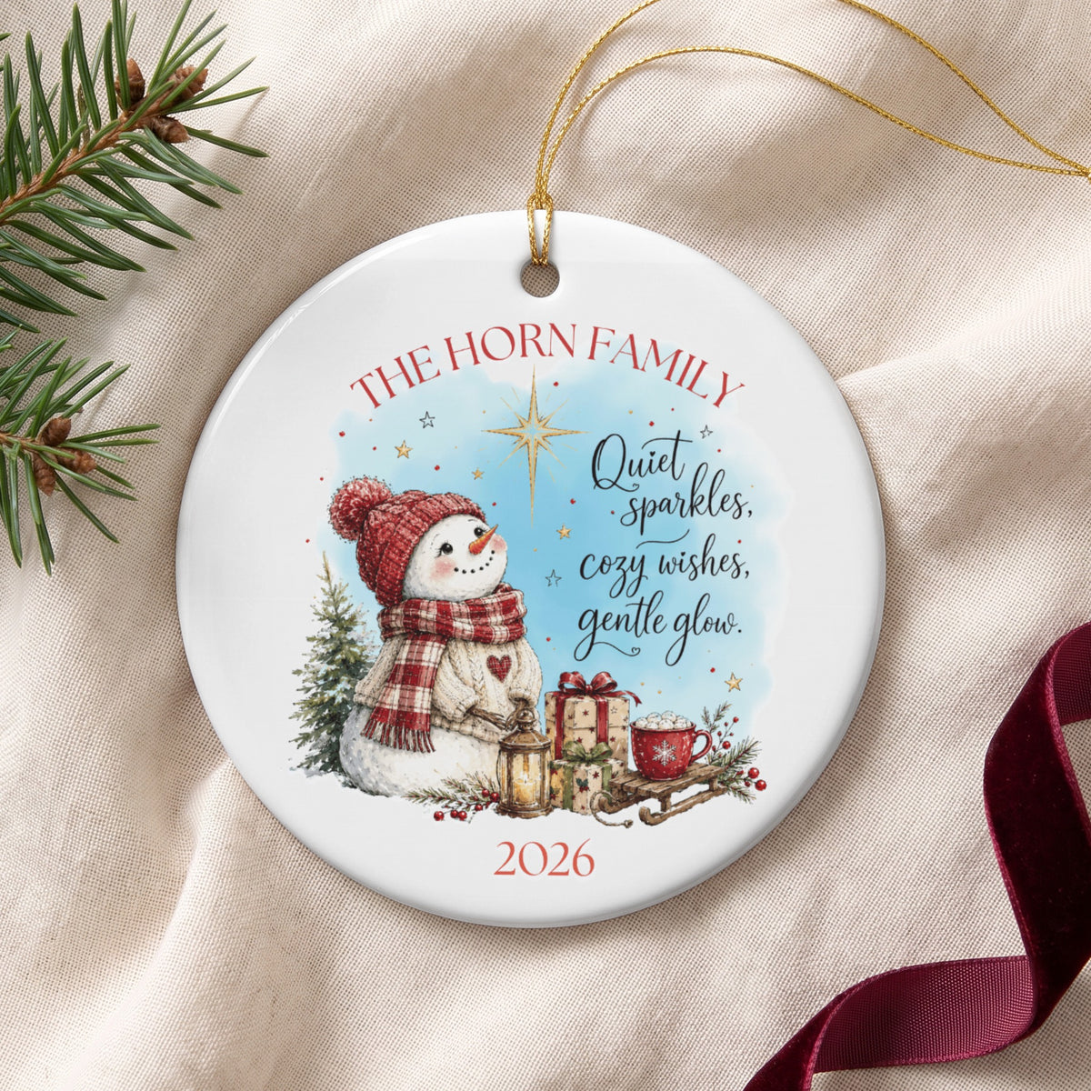 Personalized ceramic Christmas ornament featuring a watercolor snowman, gifts, and the year 2026.