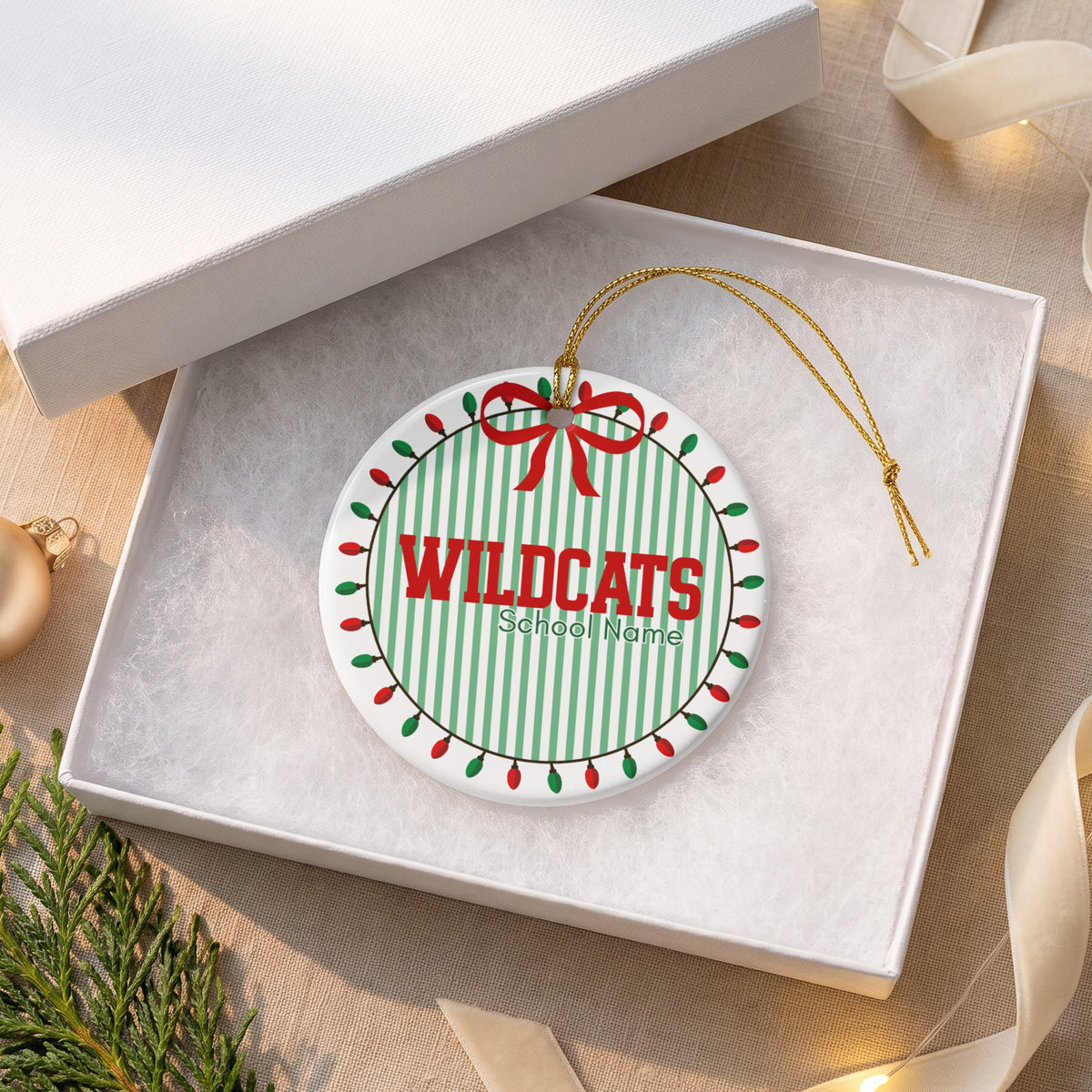 Round ornament with "WILDCATS" and "School Name" on green stripes, bordered by lights.