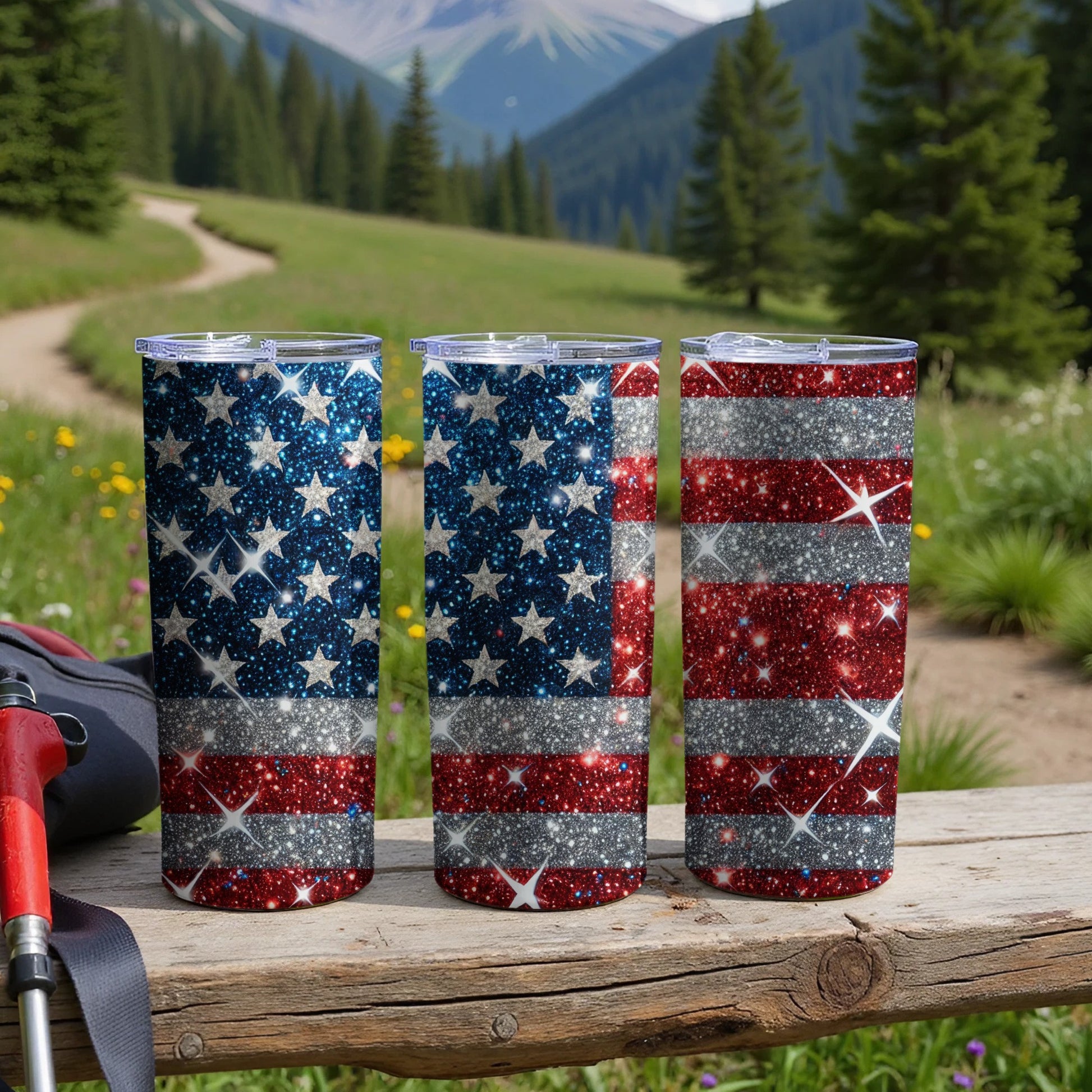 Three glittery American flag tumblers sit on a wooden surface outdoors.