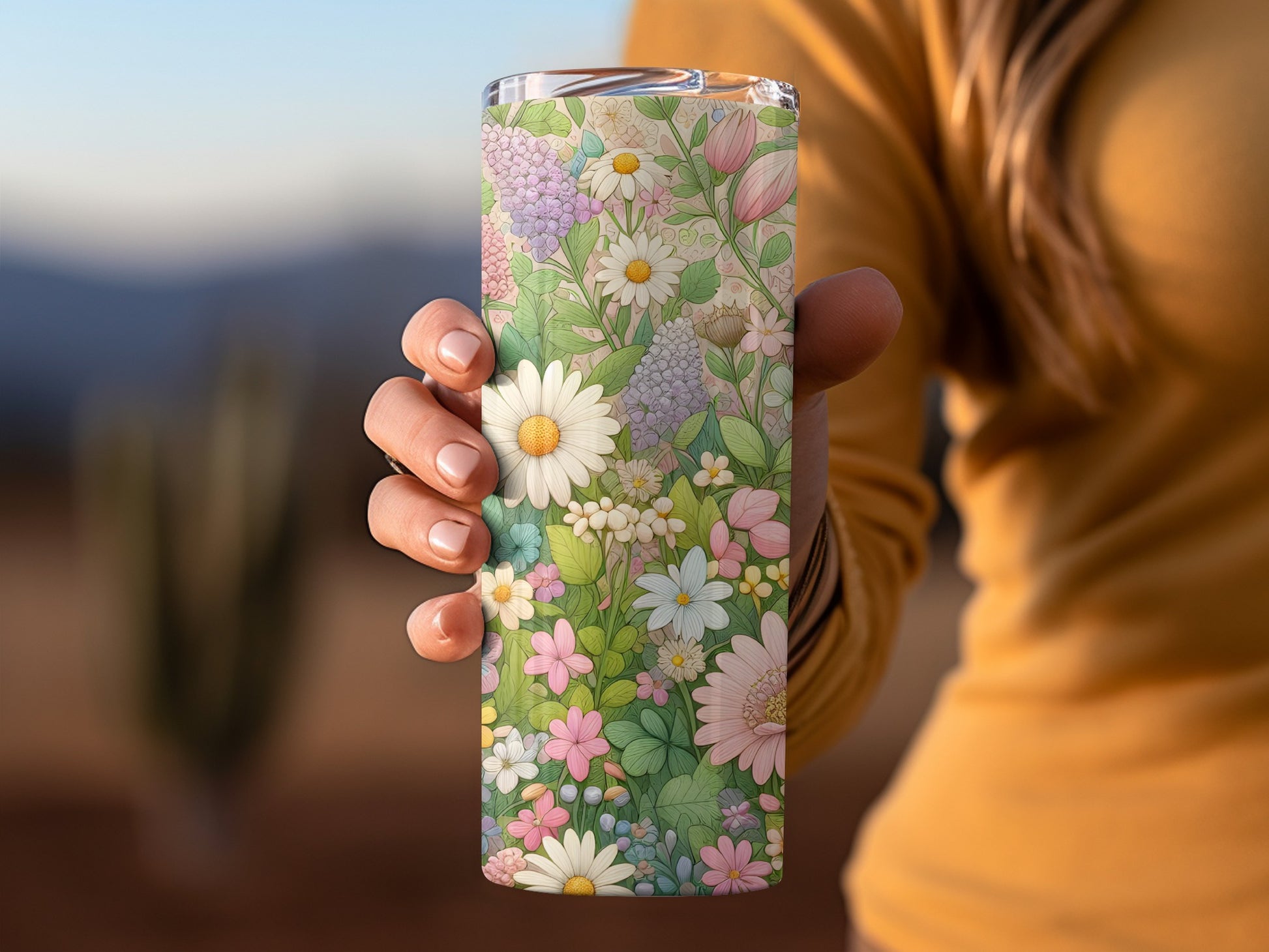 Hand holding a floral patterned tumbler with daisies and wildflowers.