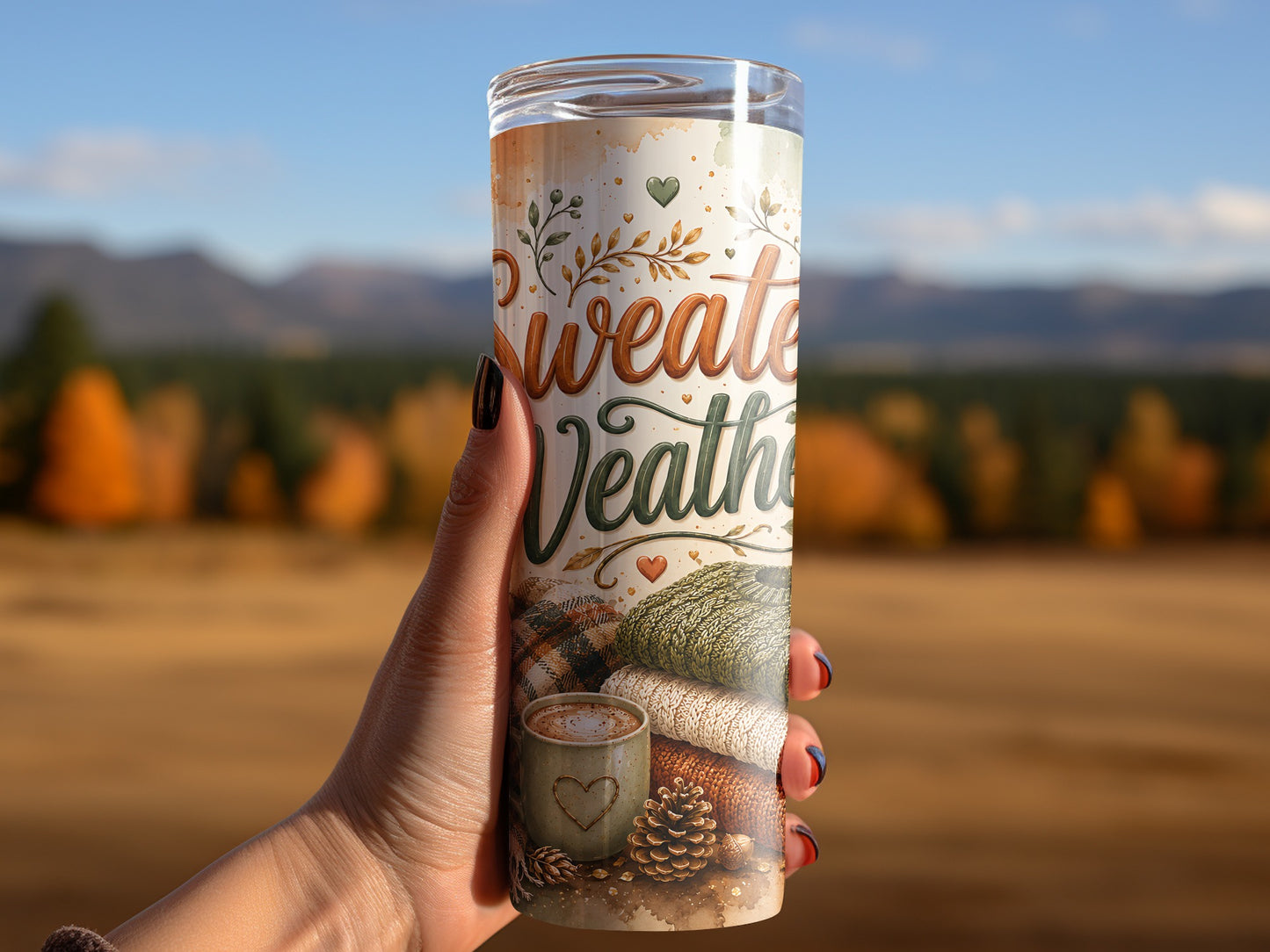 Tumbler with "Sweater Weather" text, hot cocoa, and knitted sweaters against an outdoor autumn background.