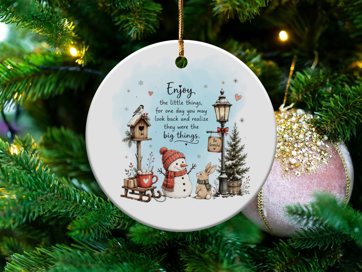 Round ceramic Christmas ornament featuring a snowman, rabbit, birdhouse, and the quote Enjoy the little things.