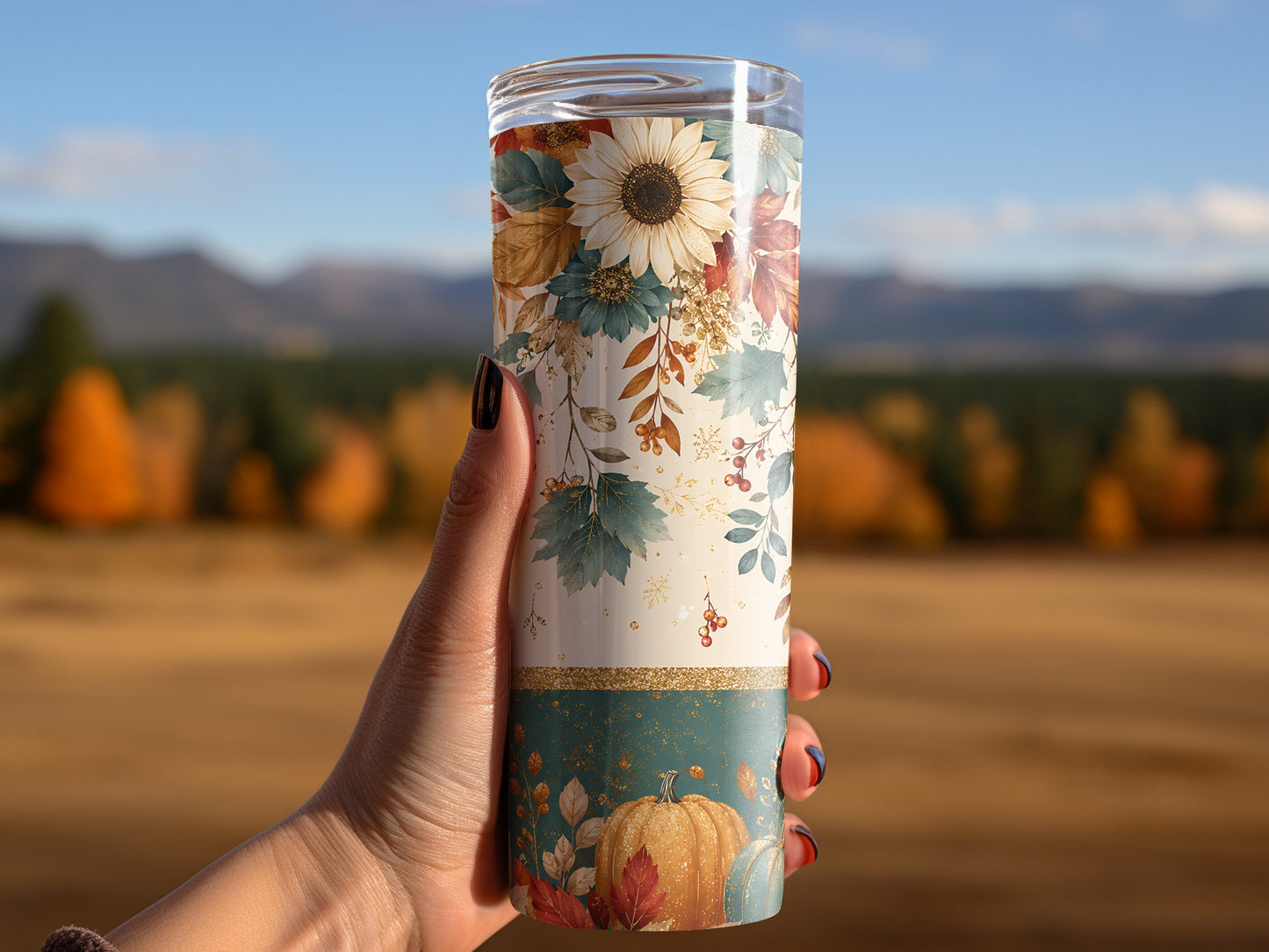 Tumbler with fall floral and pumpkin pattern held in hand outdoors.