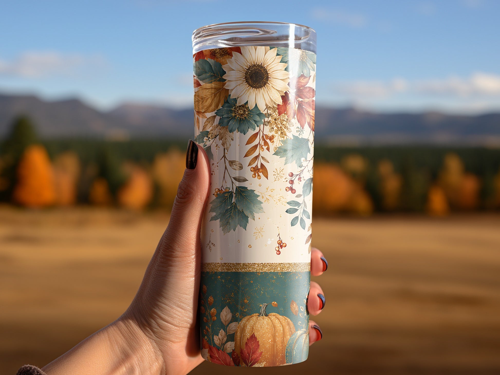 Tumbler with fall floral and pumpkin pattern held in hand outdoors.