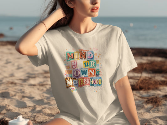 White t-shirt with "Mind Your Own Motherhood" text in colorful, blocky letters.