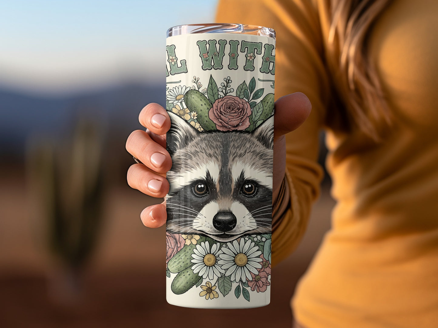 Tumbler with raccoon face, floral accents, and text "WILD WITH".