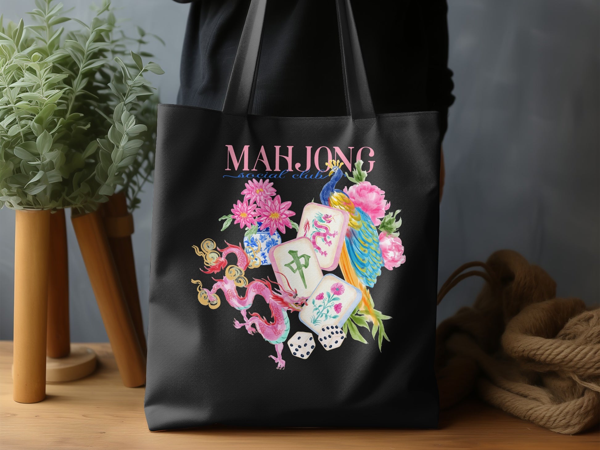 Black tote bag with "MAHJONG social club" text and watercolor dragon, peacock, and mahjong tiles.
