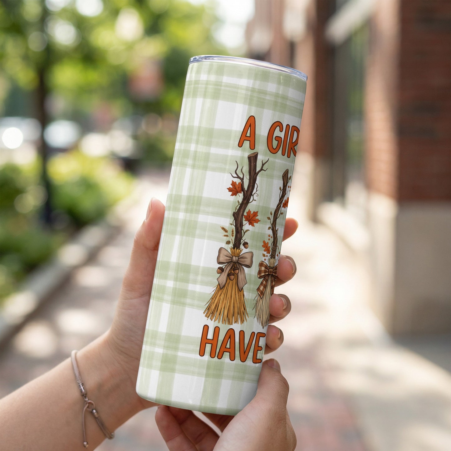 Tumbler with green plaid and "A Girl Gotta Have" text with broom and autumn leaf art.