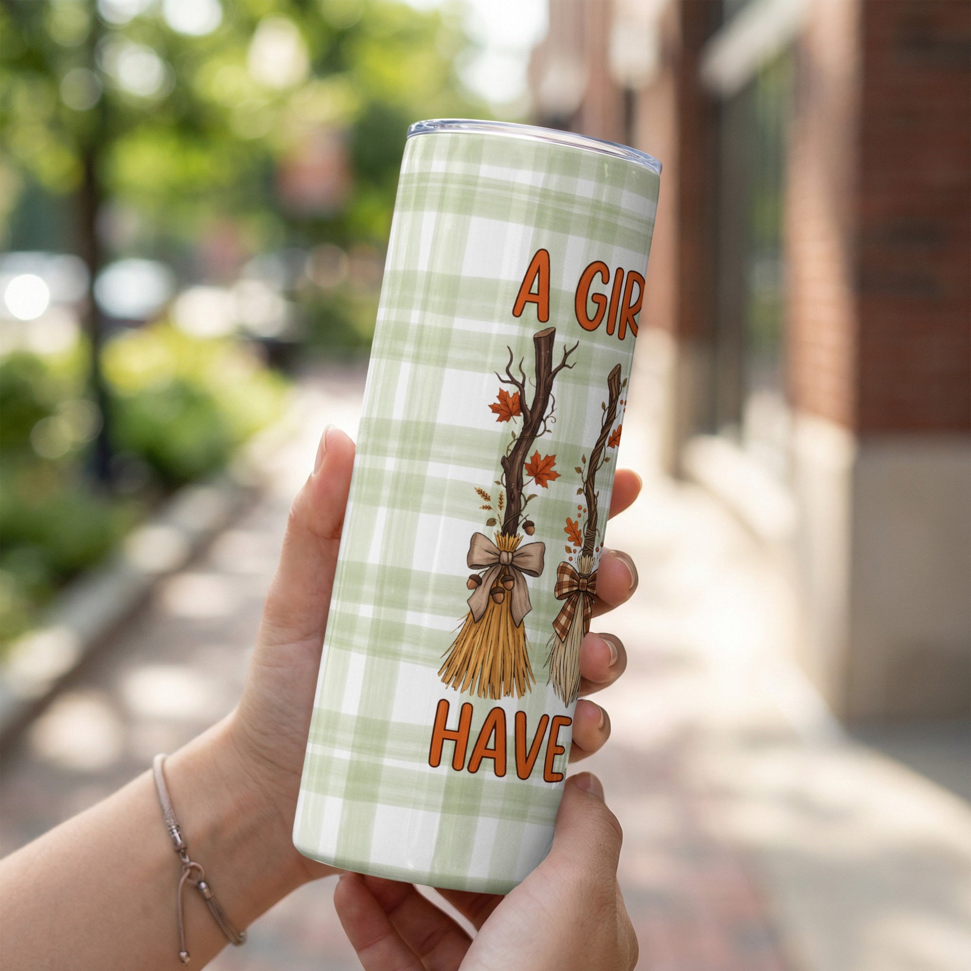 Tumbler with green plaid and "A Girl Gotta Have" text with broom and autumn leaf art.