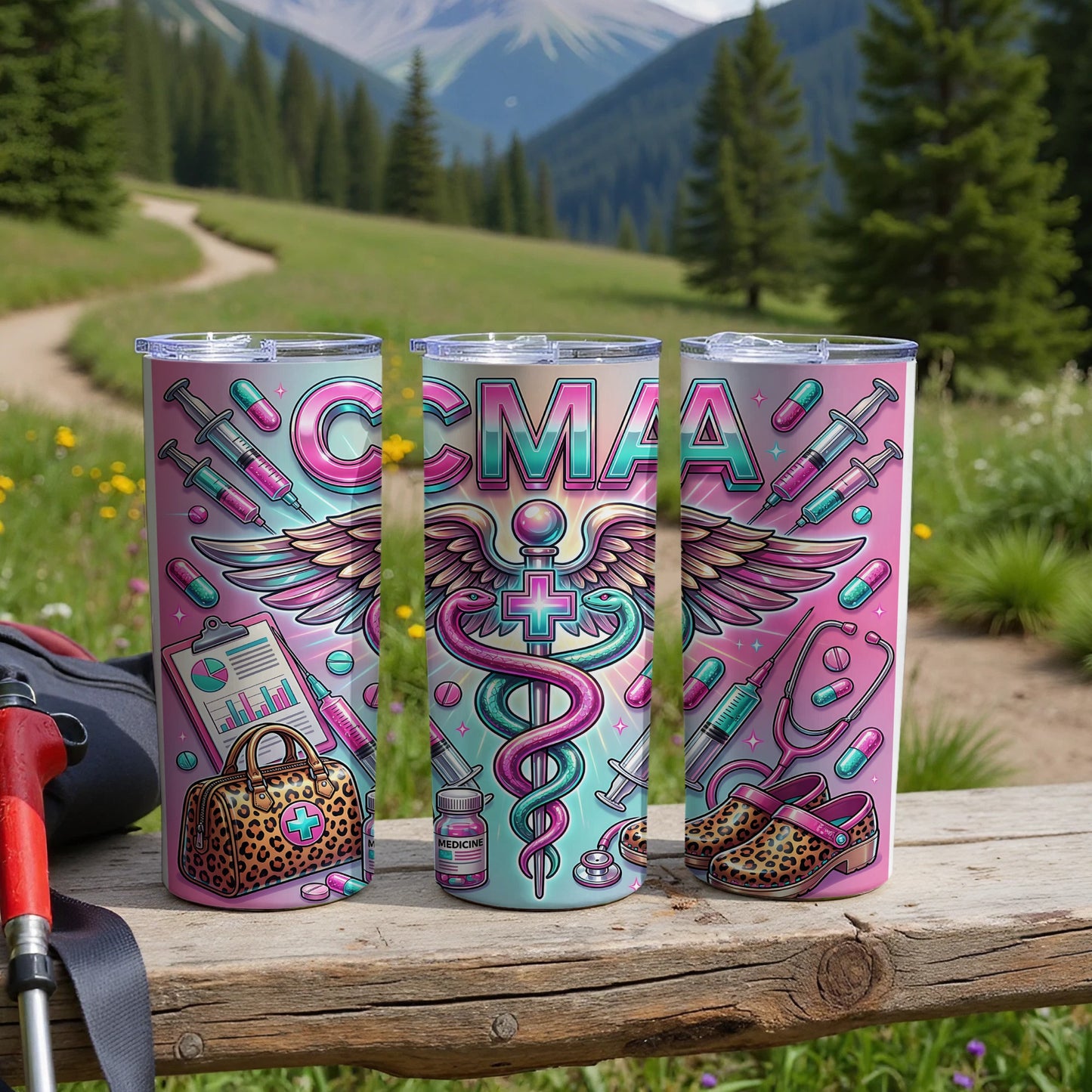 Three tumblers with CMAA logo and medical icons, set on a wooden table outdoors.