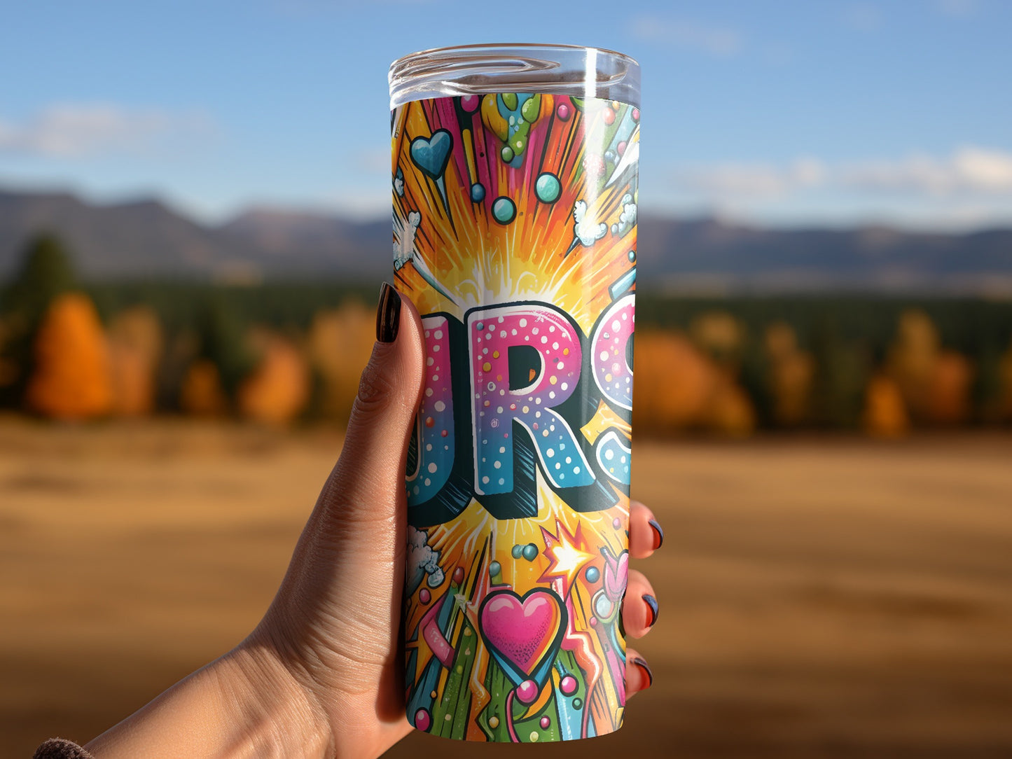 Tumbler with colorful "URG" text and hearts against a blurred natural background.
