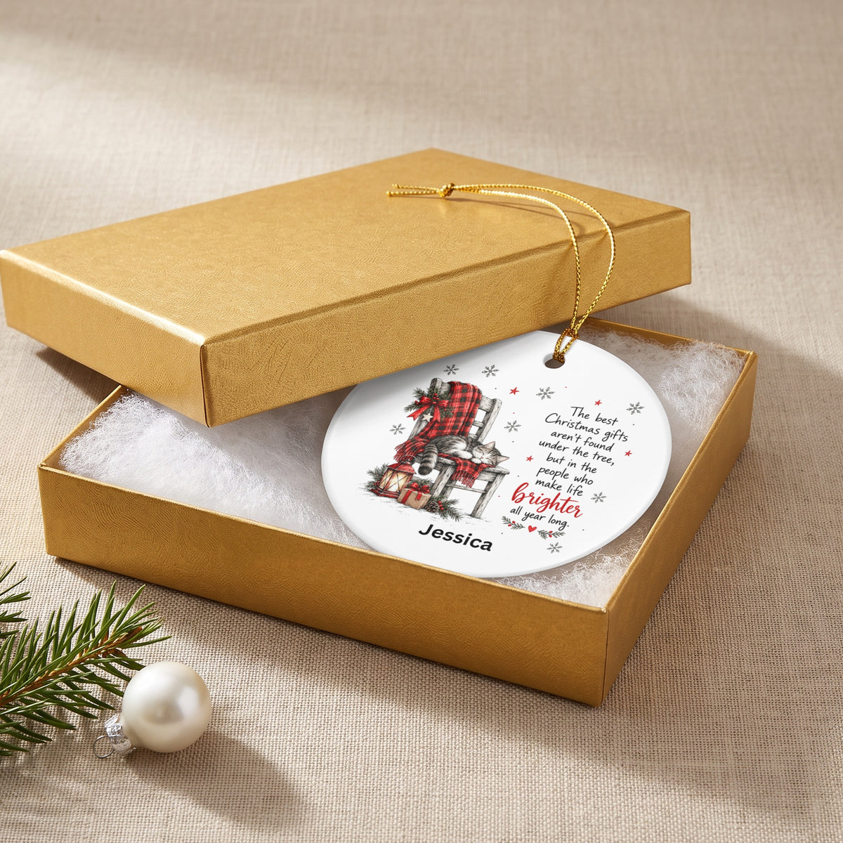 A round white ceramic Christmas ornament with a cat illustration and custom text inside a gold gift box.
