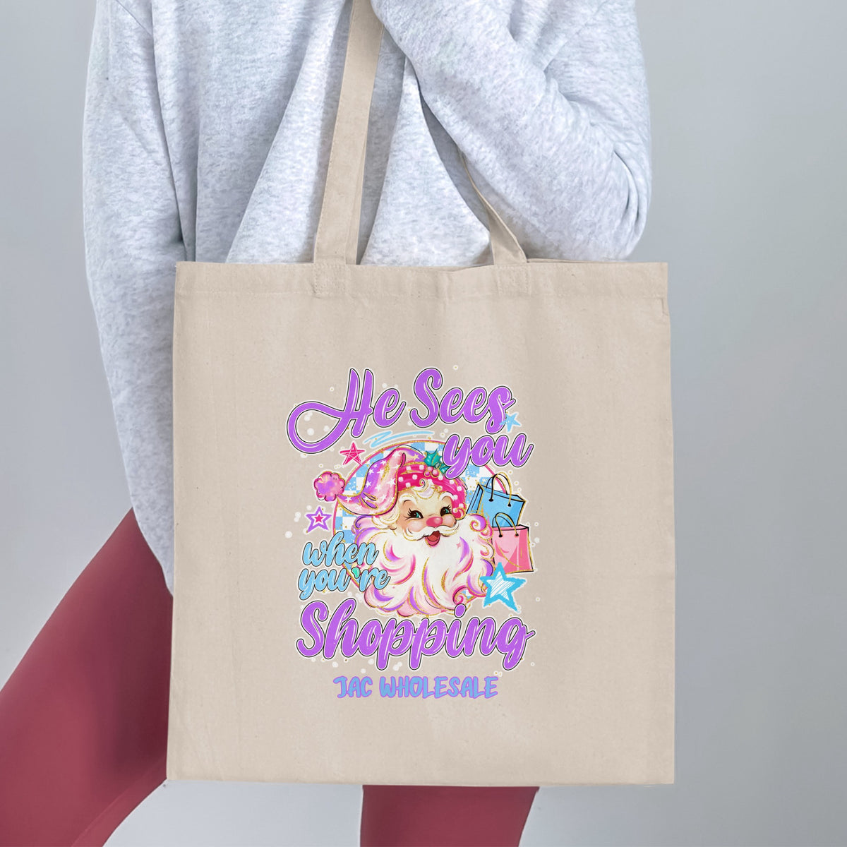 Beige tote bag with cartoon Santa, shopping bags, and text "He Sees you when you're shopping".
