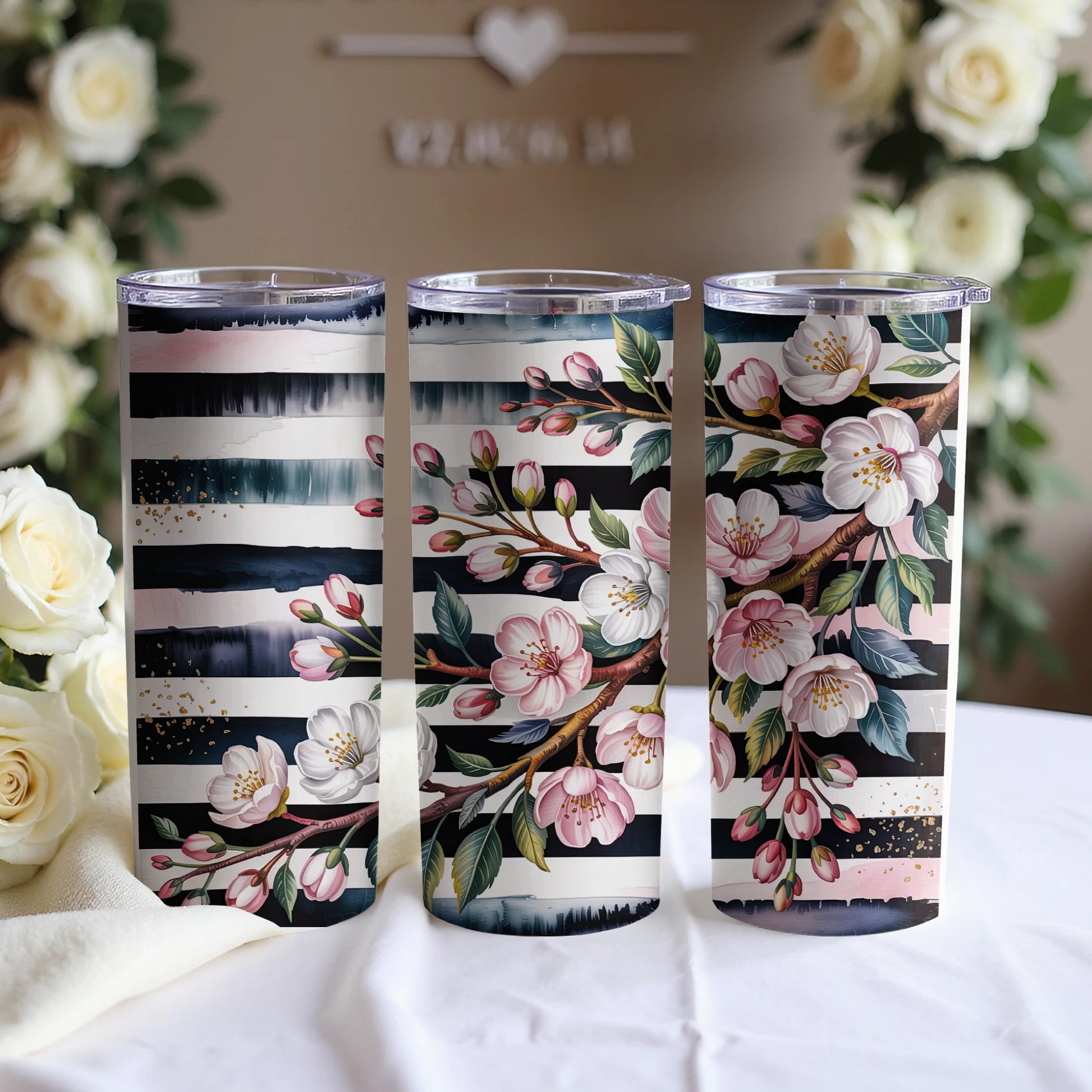 Three tumblers with floral and striped designs stand on a white cloth.