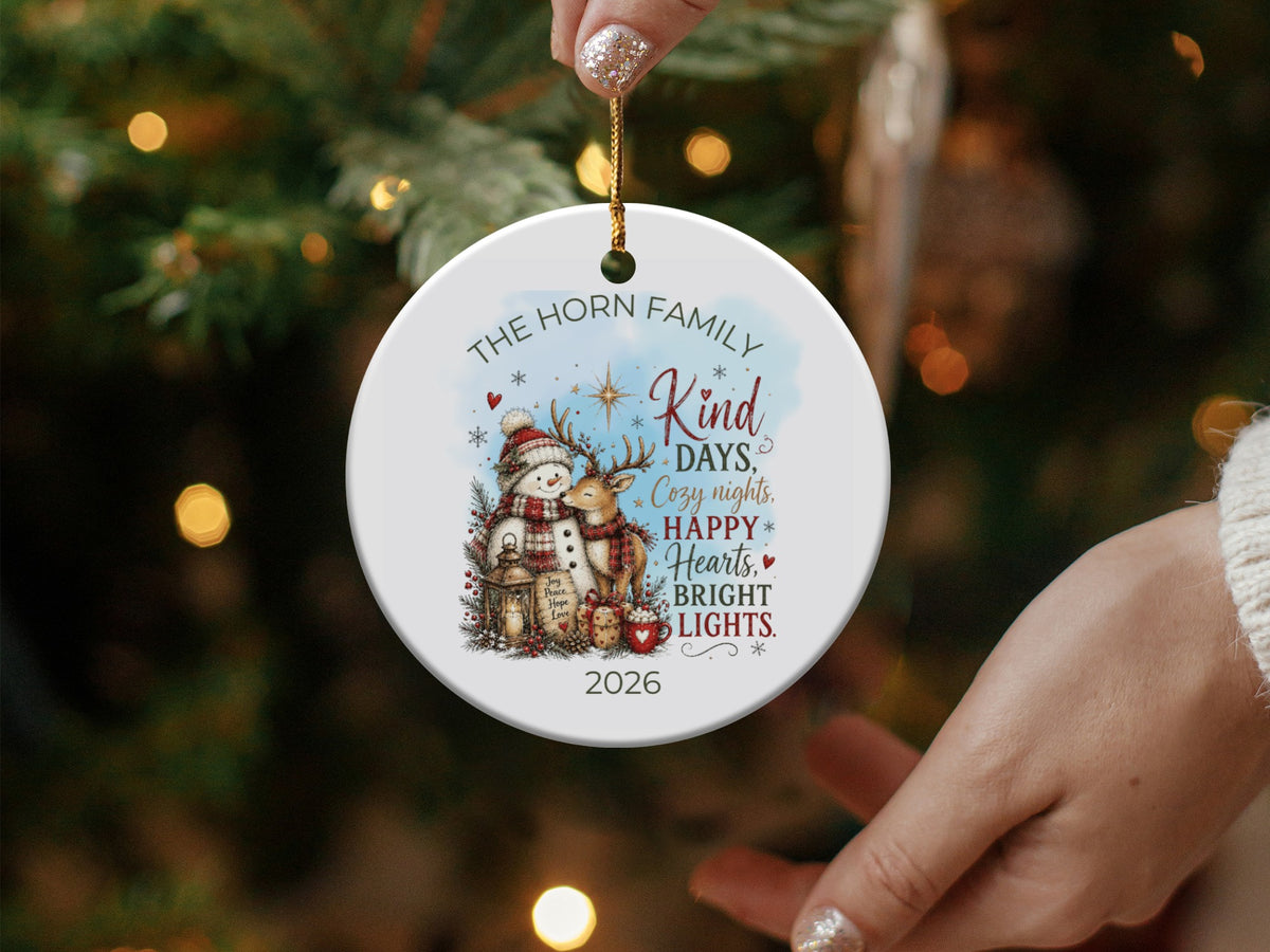 A round ceramic Christmas ornament featuring a personalized family illustration, snowman, reindeer, holiday greeting, and the year 2026.