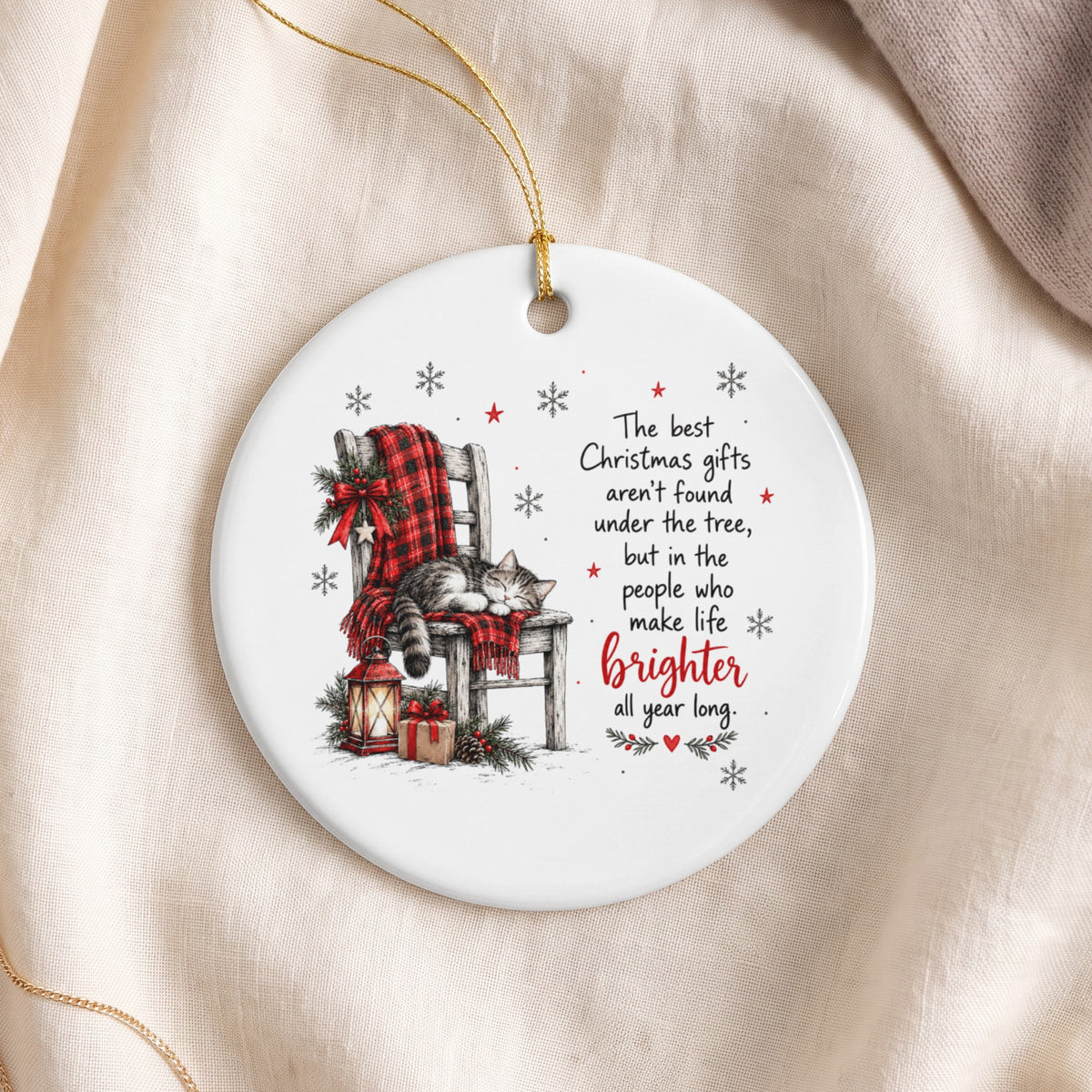 A round white ceramic Christmas ornament featuring a sleeping cat on a chair and holiday text.