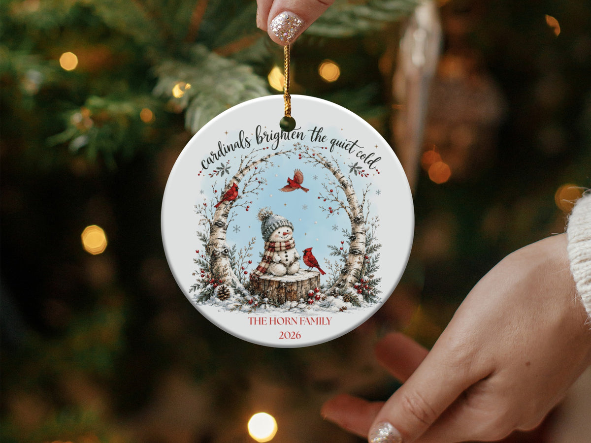 A round ceramic Christmas ornament featuring a snowman, cardinals, birch trees, and personalized text.