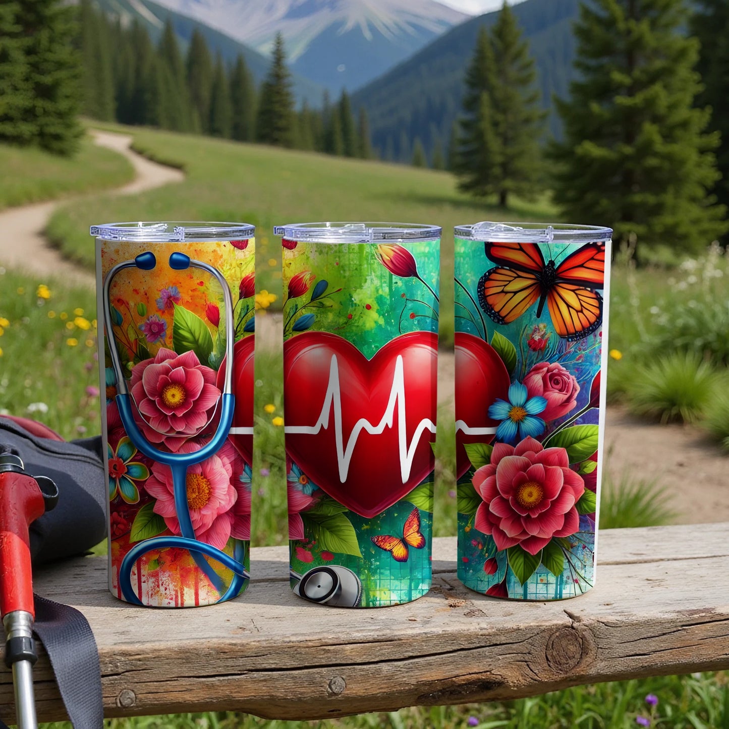 Three tumblers with floral, heart, and butterfly designs sit on a wooden surface outdoors.