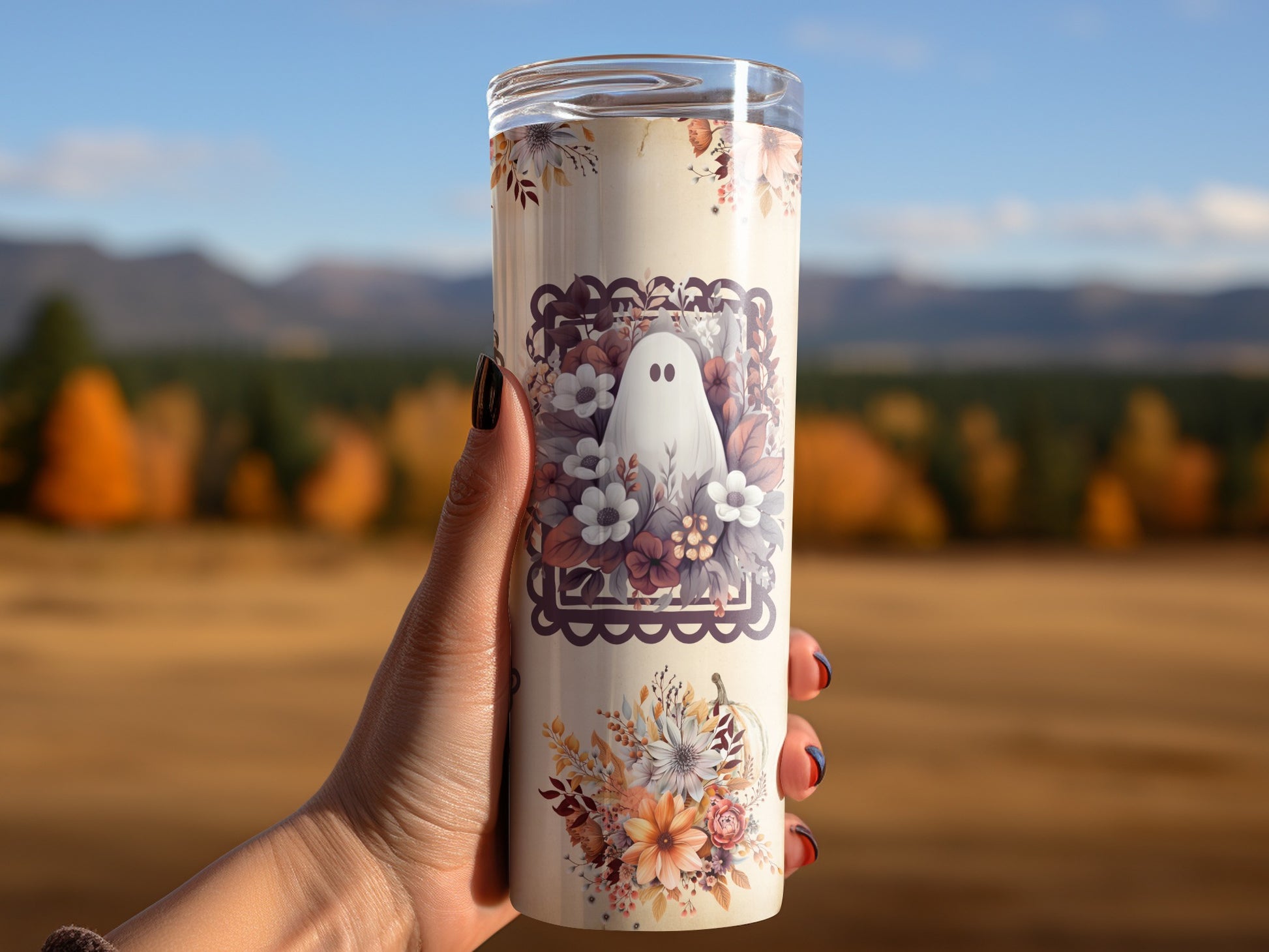 Tumbler with a ghost and floral design held outdoors with autumn scenery.