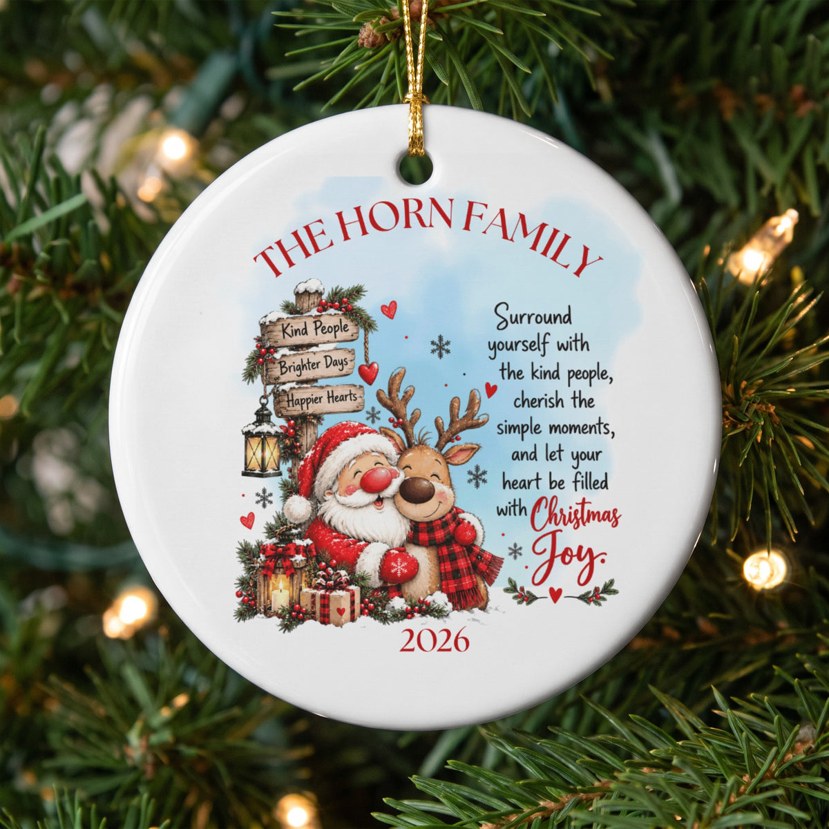 A round white Christmas ornament hanging on a tree features Santa and a reindeer hugging near a signpost with family text and the year 2026.