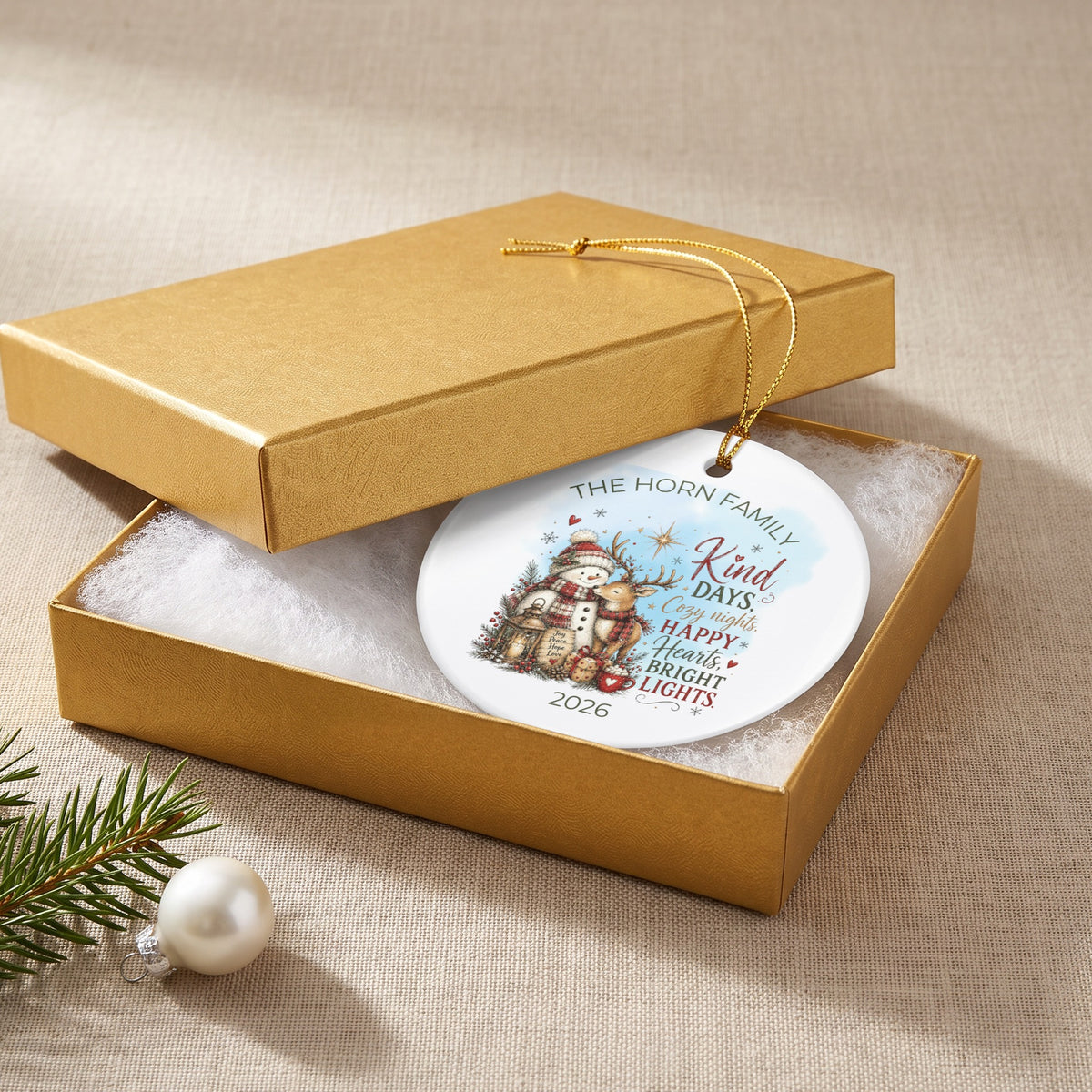 A personalized round white Christmas ornament rests in an open gold gift box.