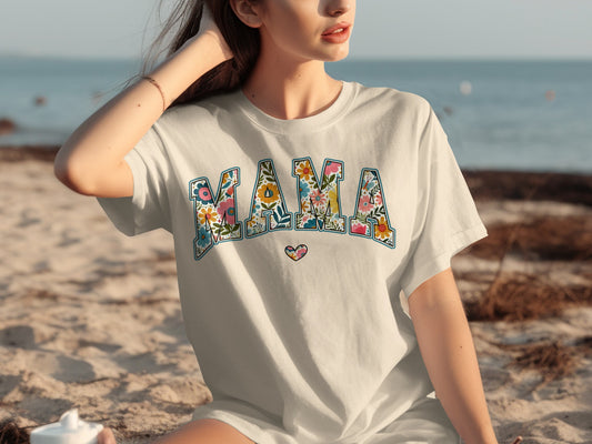 White t-shirt with "MAMA" in floral letters, on a woman at the beach.