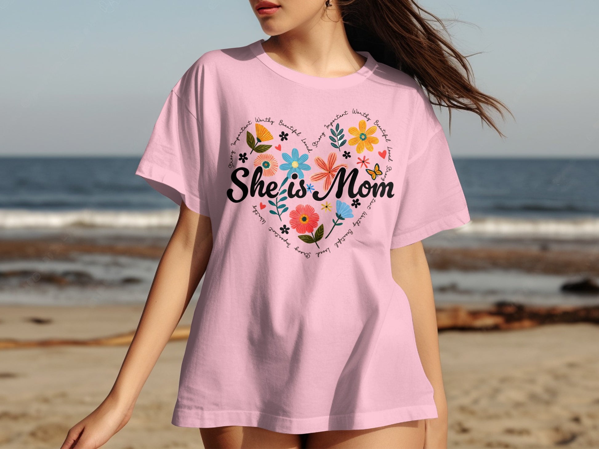 Pink t-shirt with "She is Mom" and floral heart design.