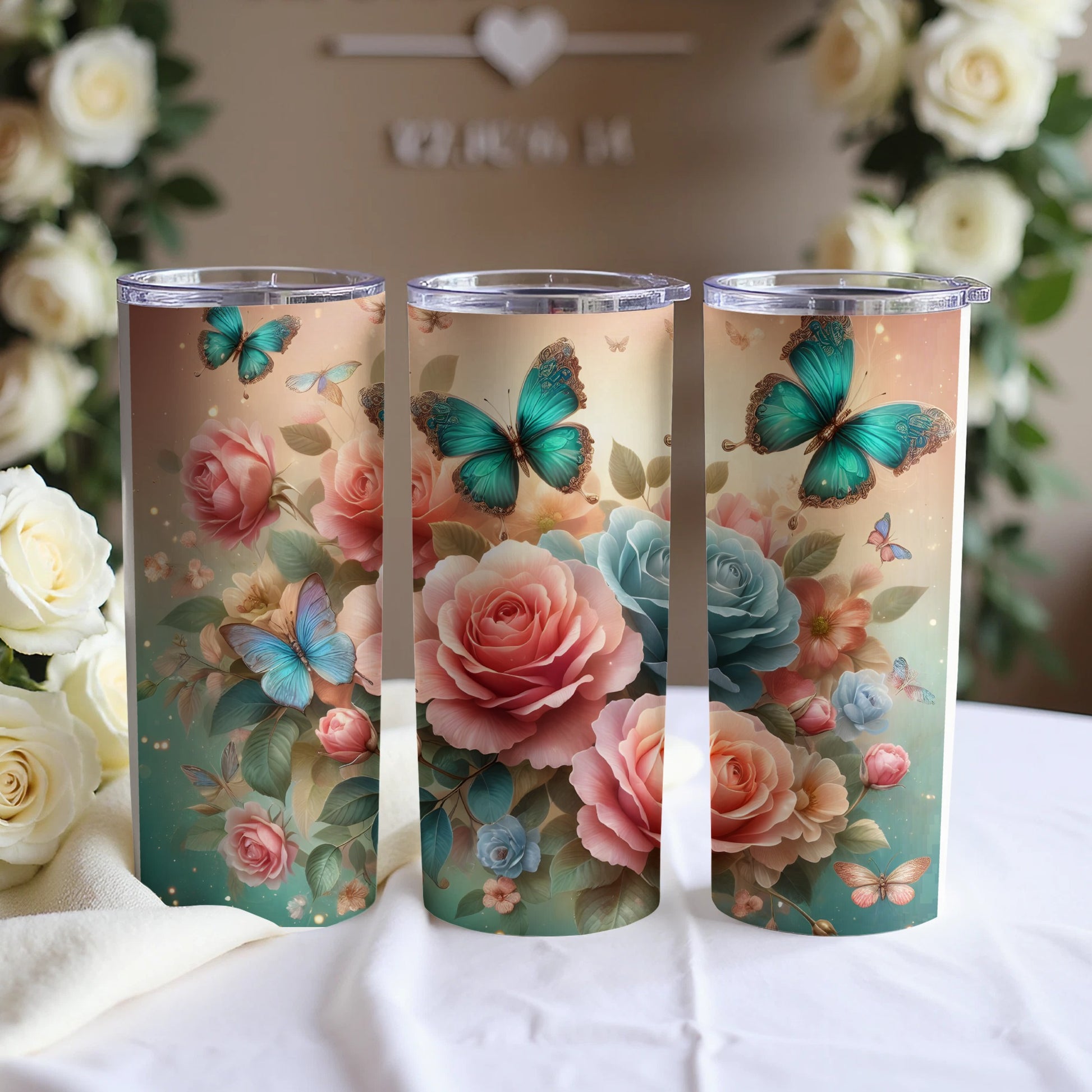 Three tumblers decorated with butterflies and roses, displayed on a table.