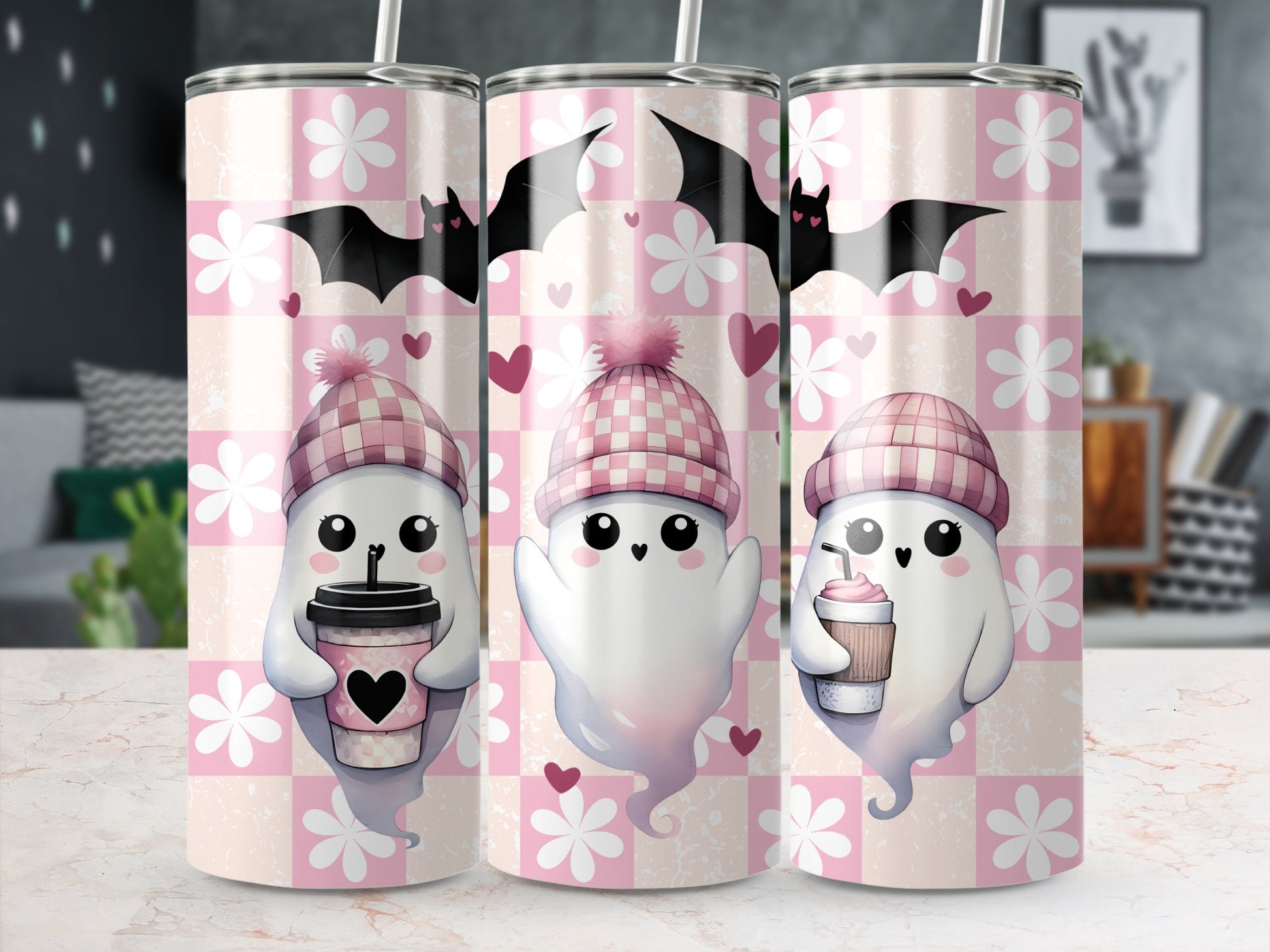Three tumblers with cute ghosts holding drinks, bats, and hearts on a pink checkered pattern.