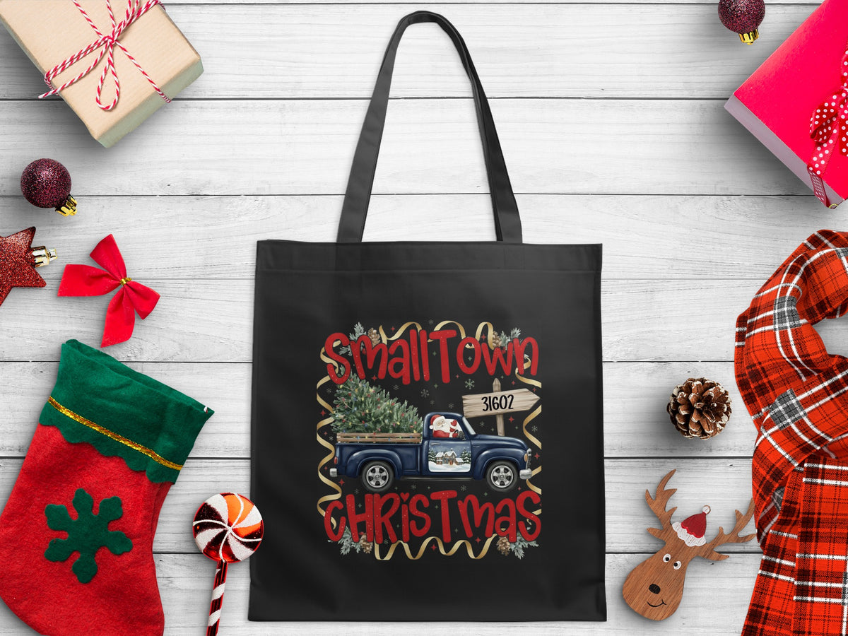 Black tote bag with "Small Town Christmas" design featuring a blue truck with a Christmas tree.
