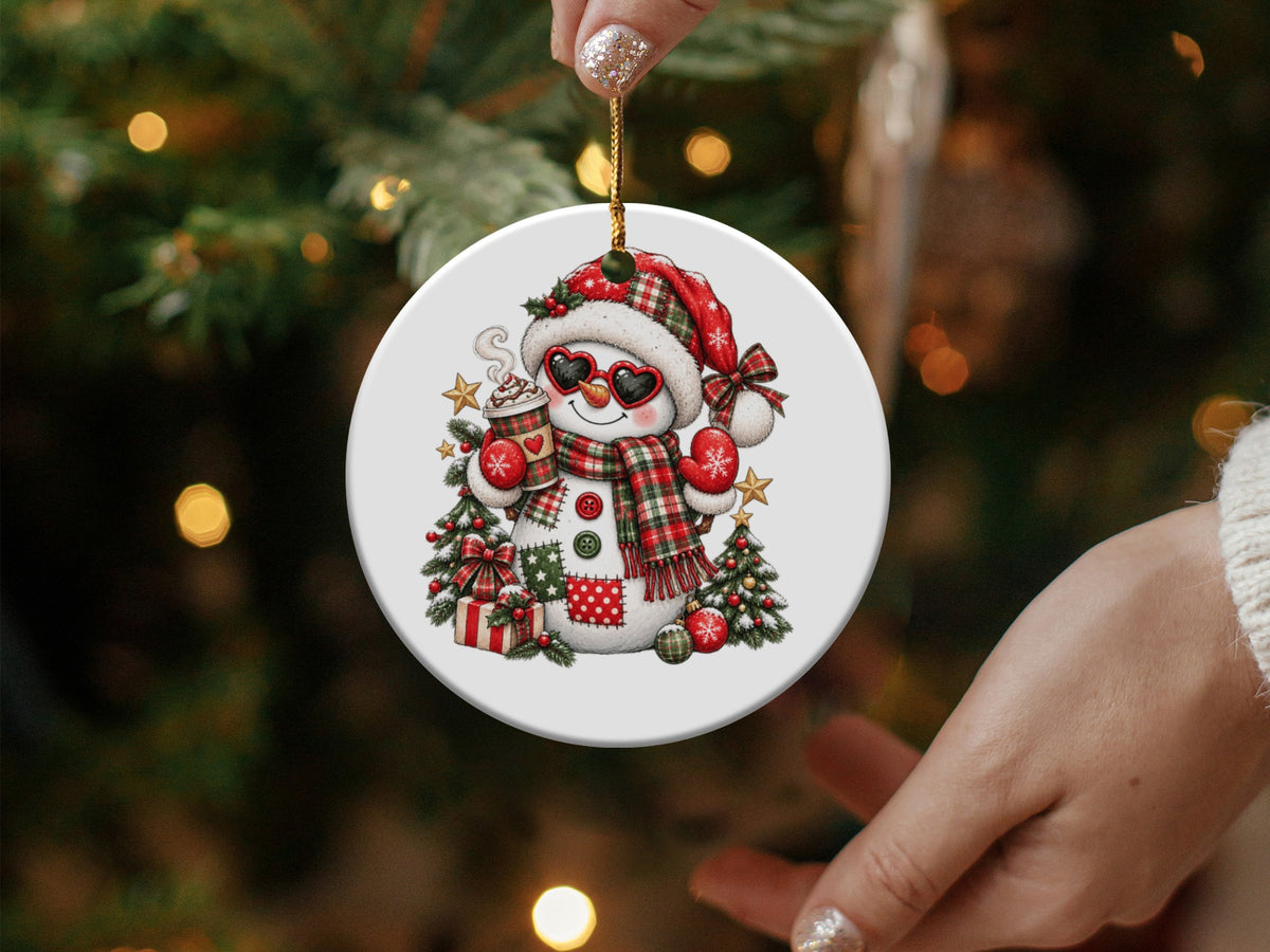 Round Christmas ornament featuring a snowman holding a hot drink and wearing a plaid hat and scarf.