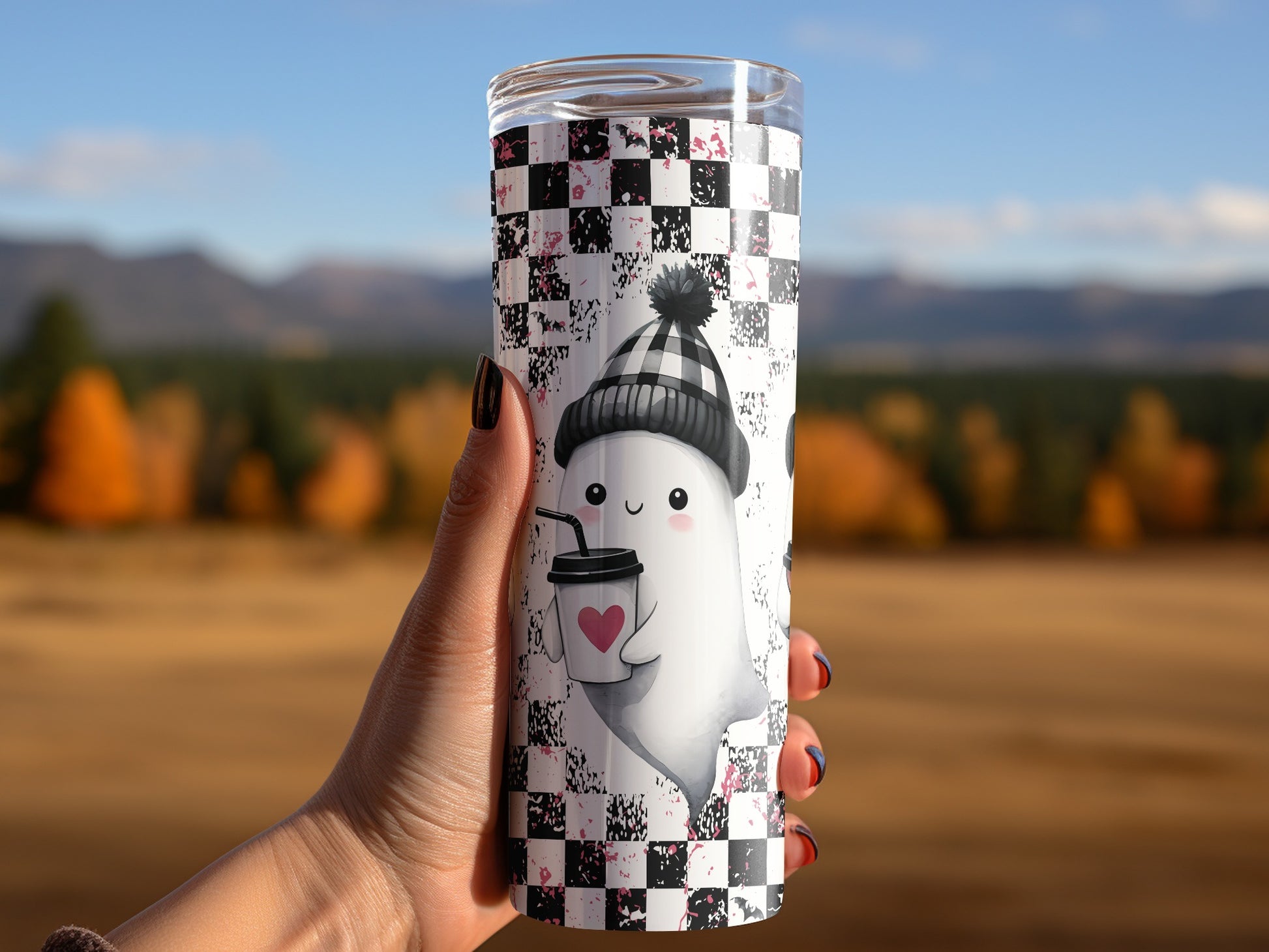Tumbler with cute ghost holding coffee cup on black and white checkered background.