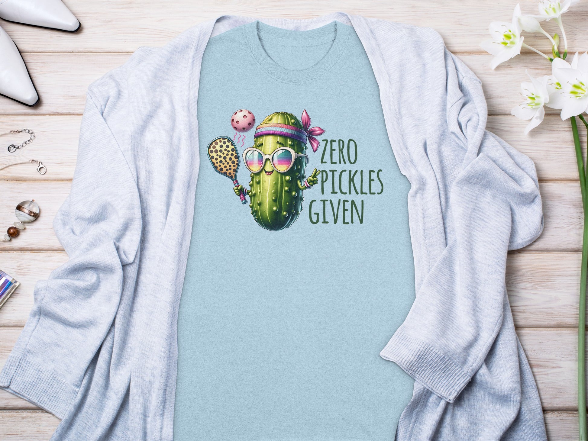 Light blue t-shirt with a cartoon pickle holding a pickleball paddle and ball, text reads "ZERO PICKLES GIVEN."