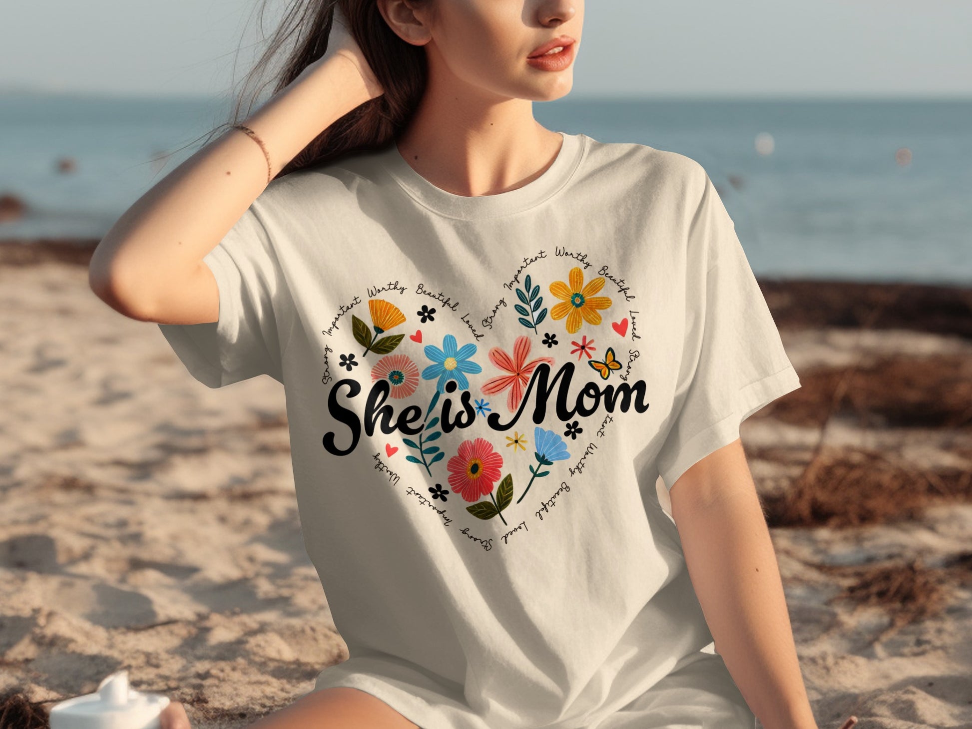 White t-shirt with "She is Mom" and floral heart graphic.