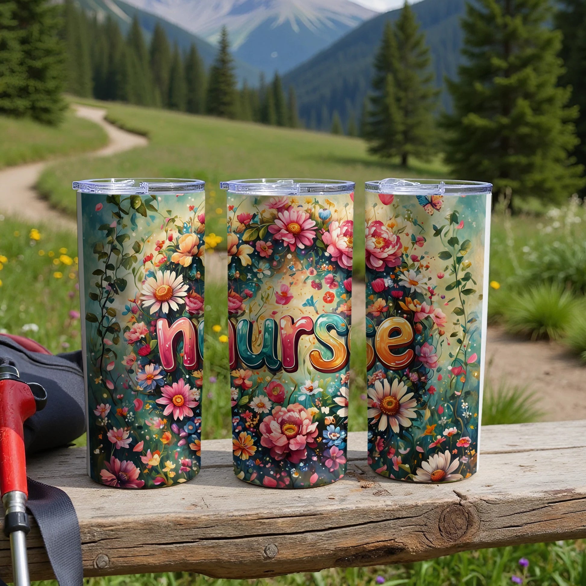 Three floral nurse tumblers lined up on a wooden surface with a scenic mountain background.