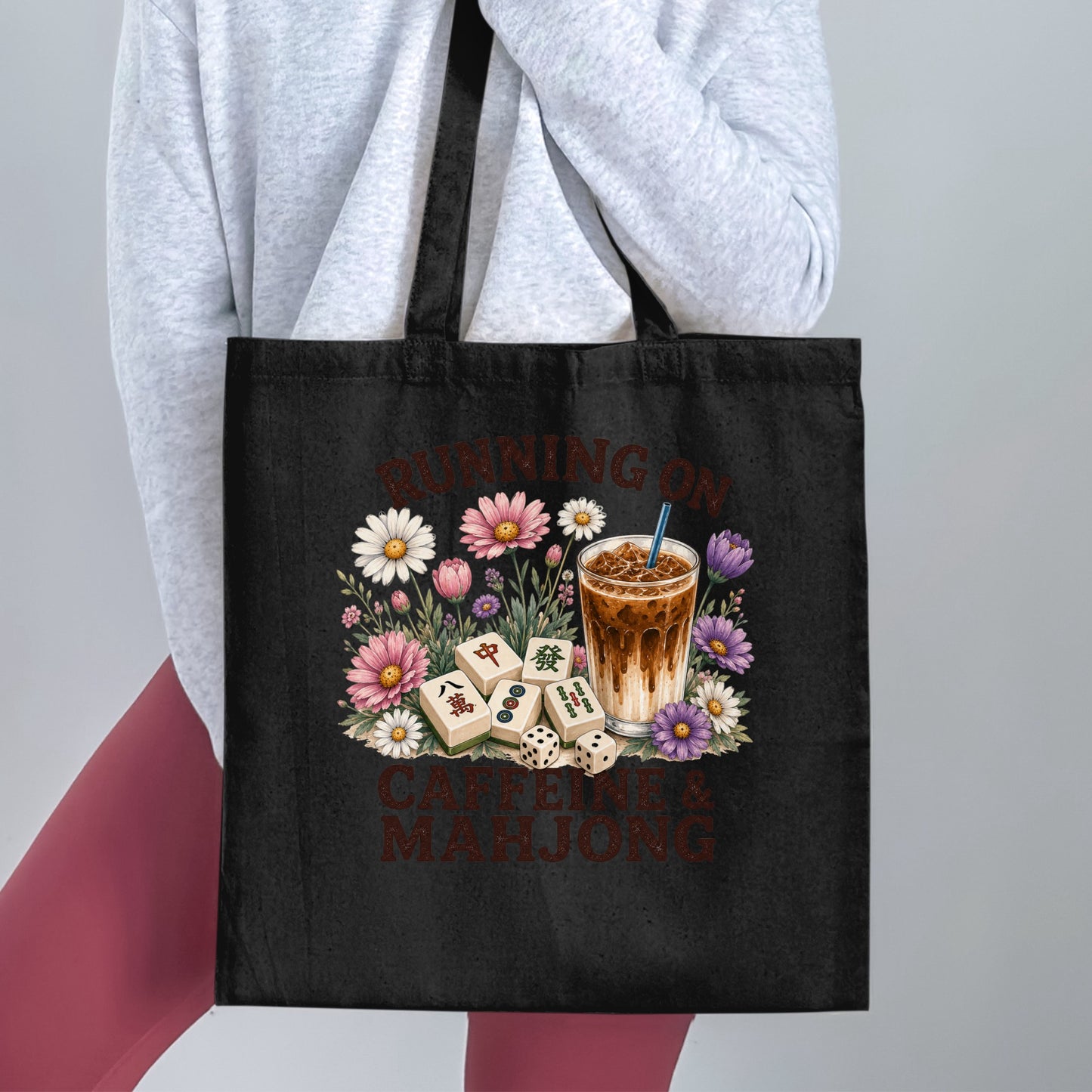 Black tote bag with "Running on Caffeine & Mahjong" text and floral design.