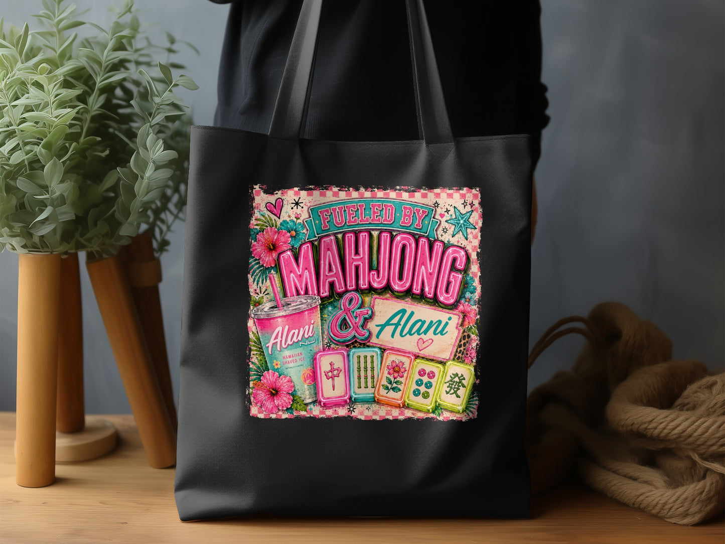 Black tote bag with "Fueled by Mahjong & Alani" Hawaiian Shaved Ice graphic.