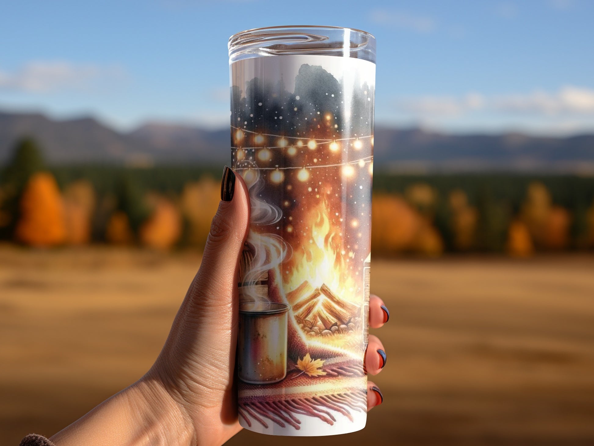 Tumbler with campfire, string lights, and hot drink design held outdoors.